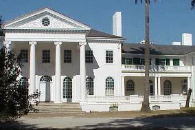 A front view of the two-story, white Plum Orchard Mansion with a large portico and classic columns.