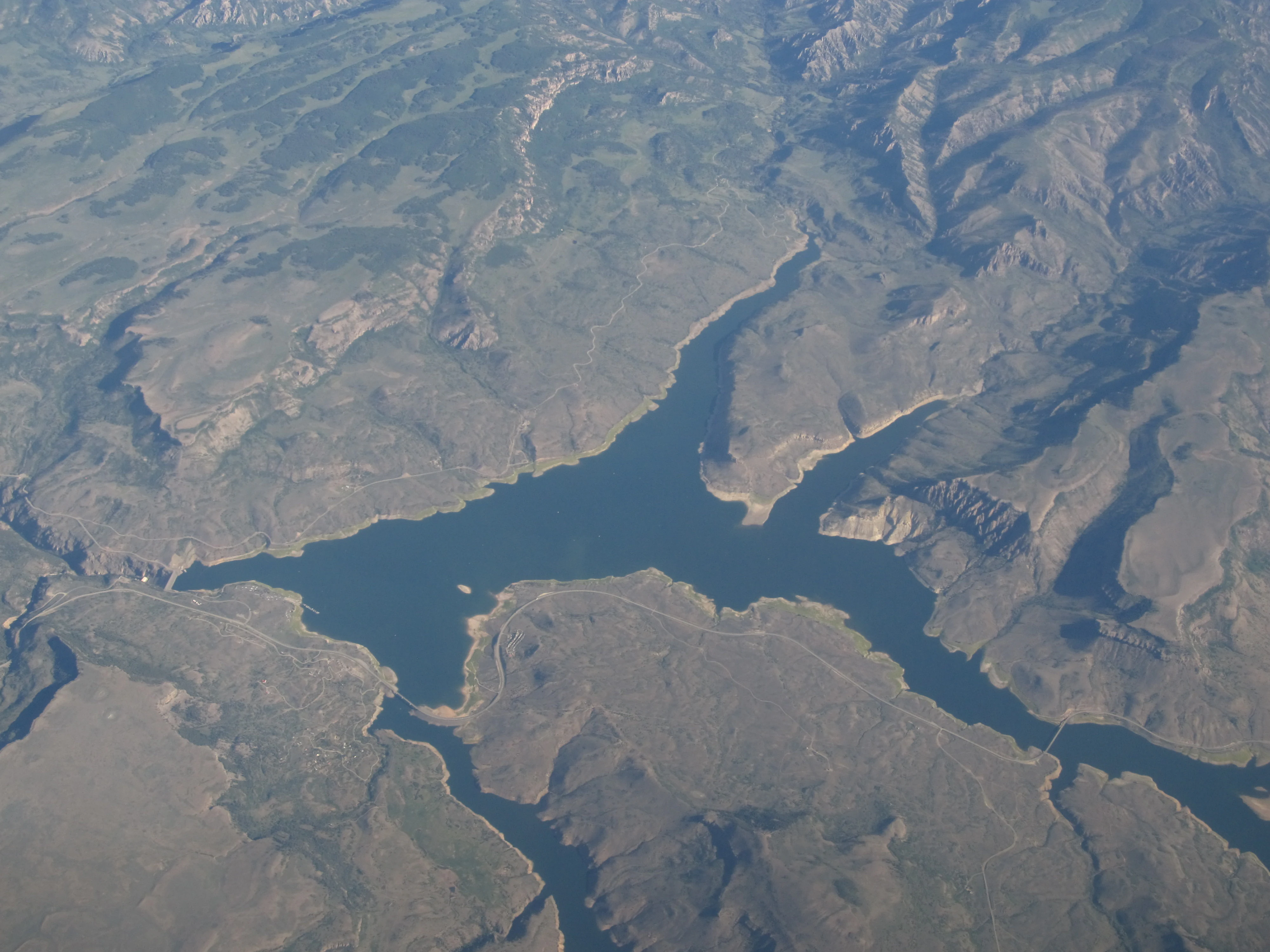 An aerial photograph looking down at the winding, dark blue reservoirs of the Gunnison River set within rugged, arid canyon terrain in Colorado.