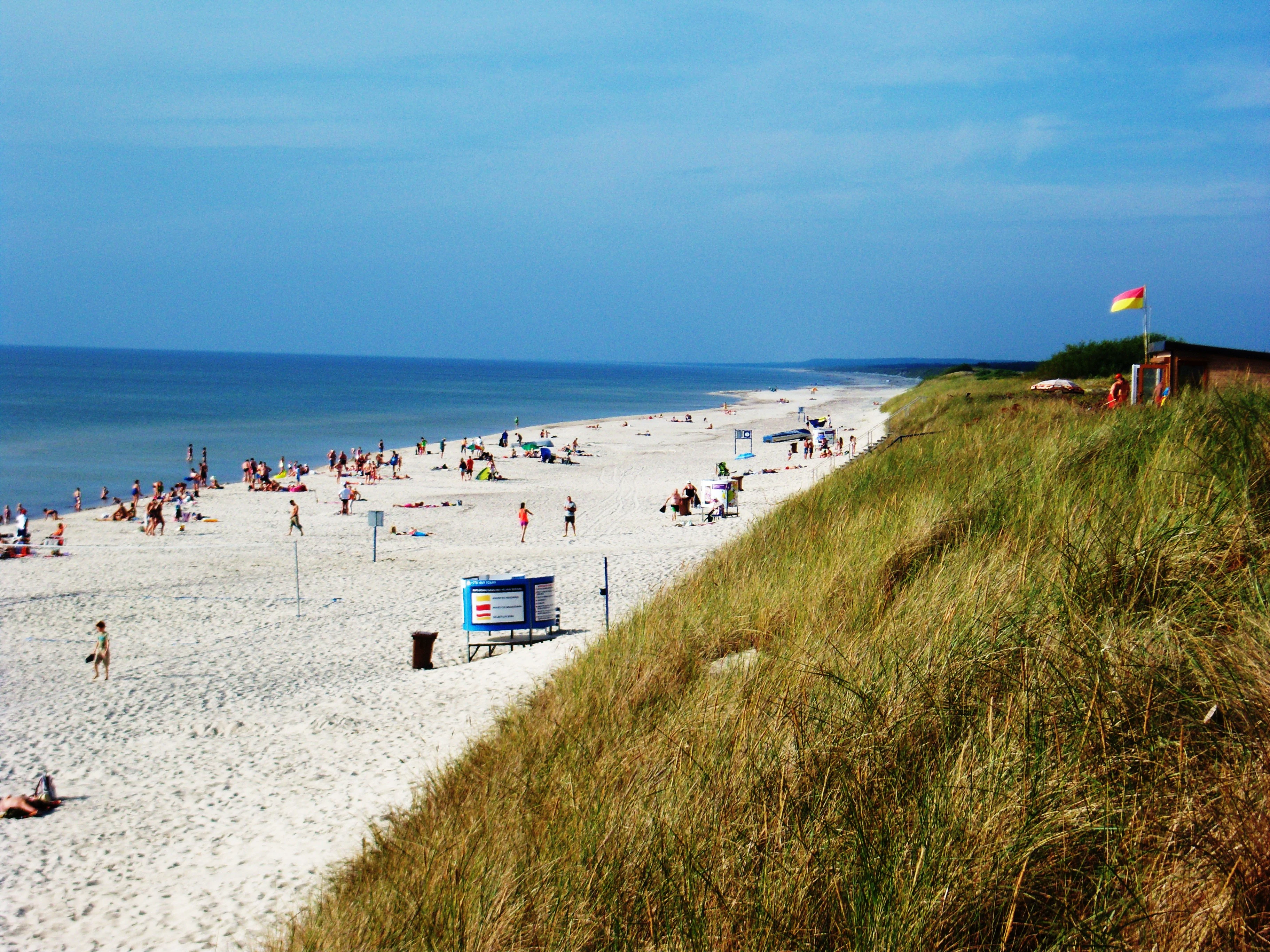 White sandy beach along the Baltic Sea with grass-covered dunes, people, and a clear blue sky