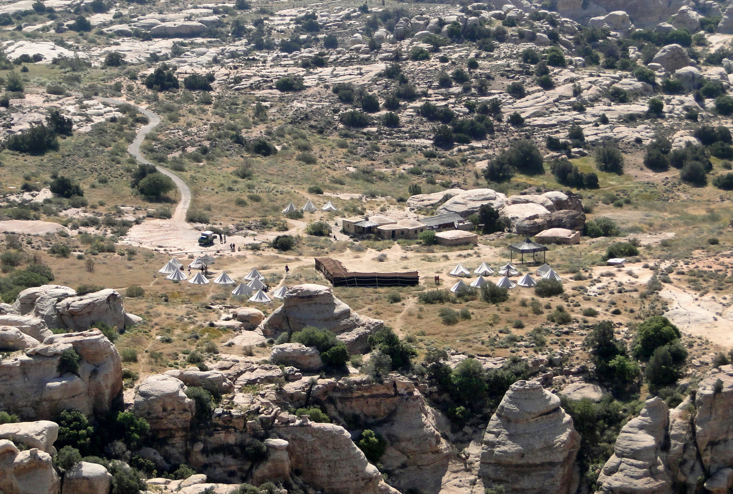 Wide aerial view of Rummana Campsite with white tents, rocky terrain, and scattered structures in Dana Biosphere Reserve