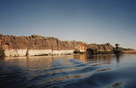 River flowing through a limestone gorge with steep cliffs in the background under clear blue sky