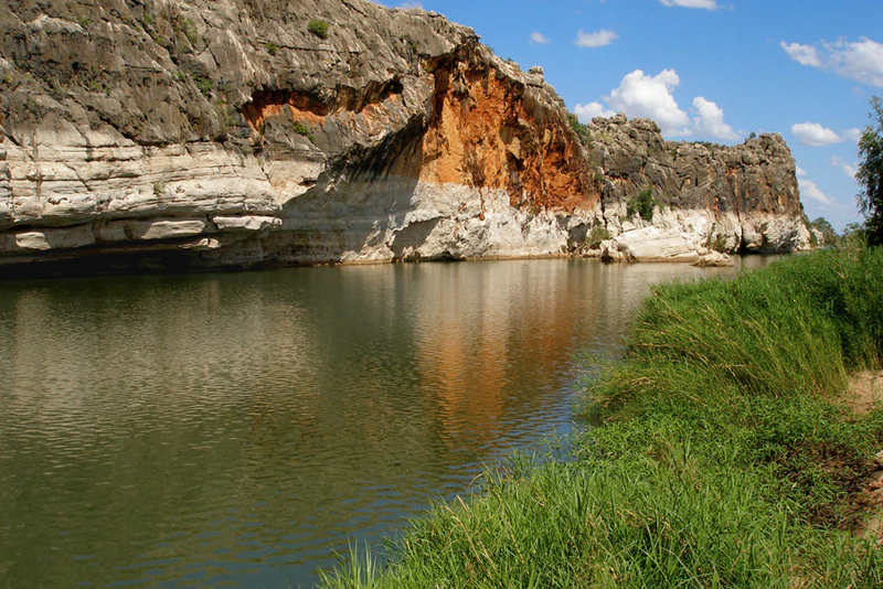 Calm river reflecting limestone cliffs and green vegetation on the riverbank under a clear blue sky