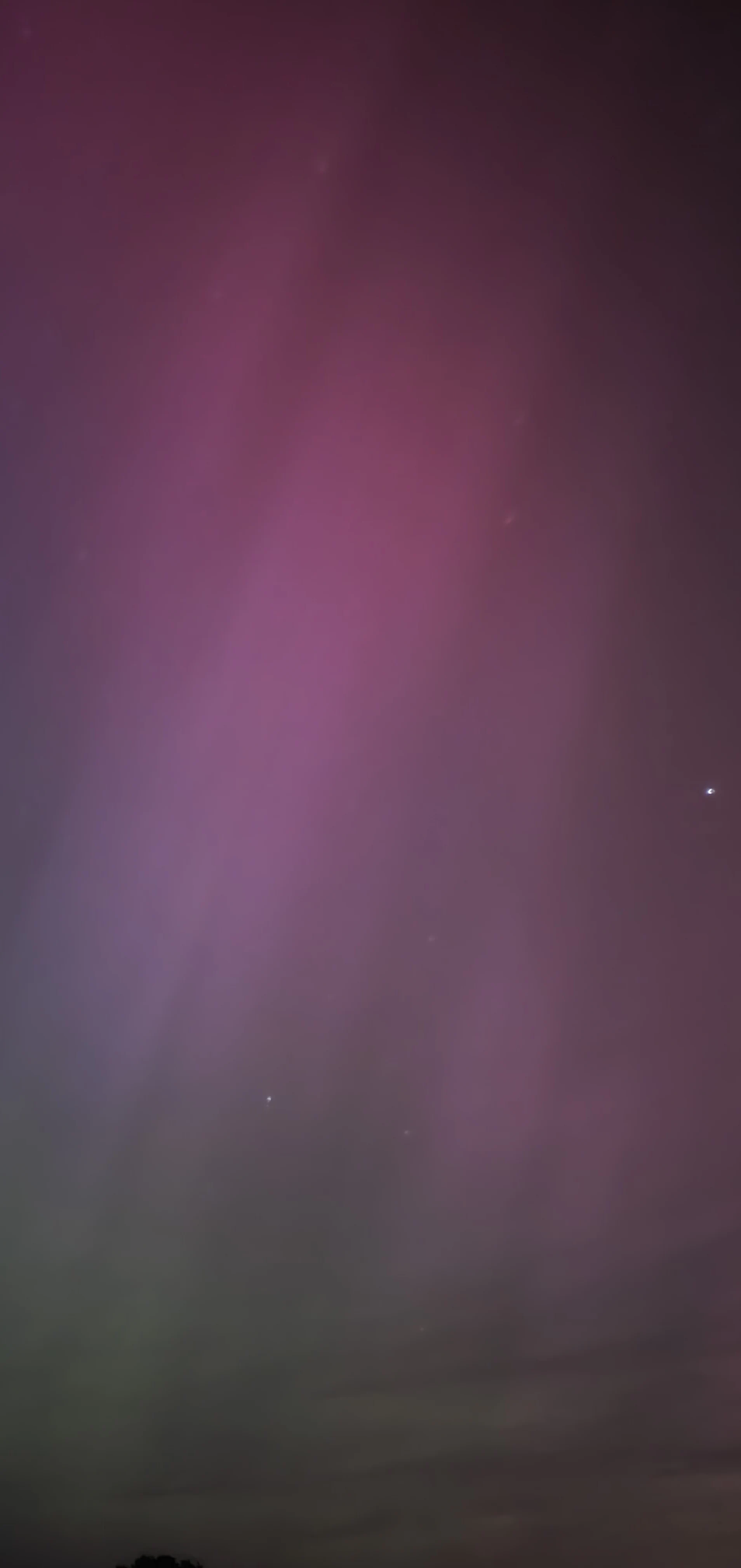 Night sky with purple and green aurora borealis, faint stars visible, dark landscape silhouette