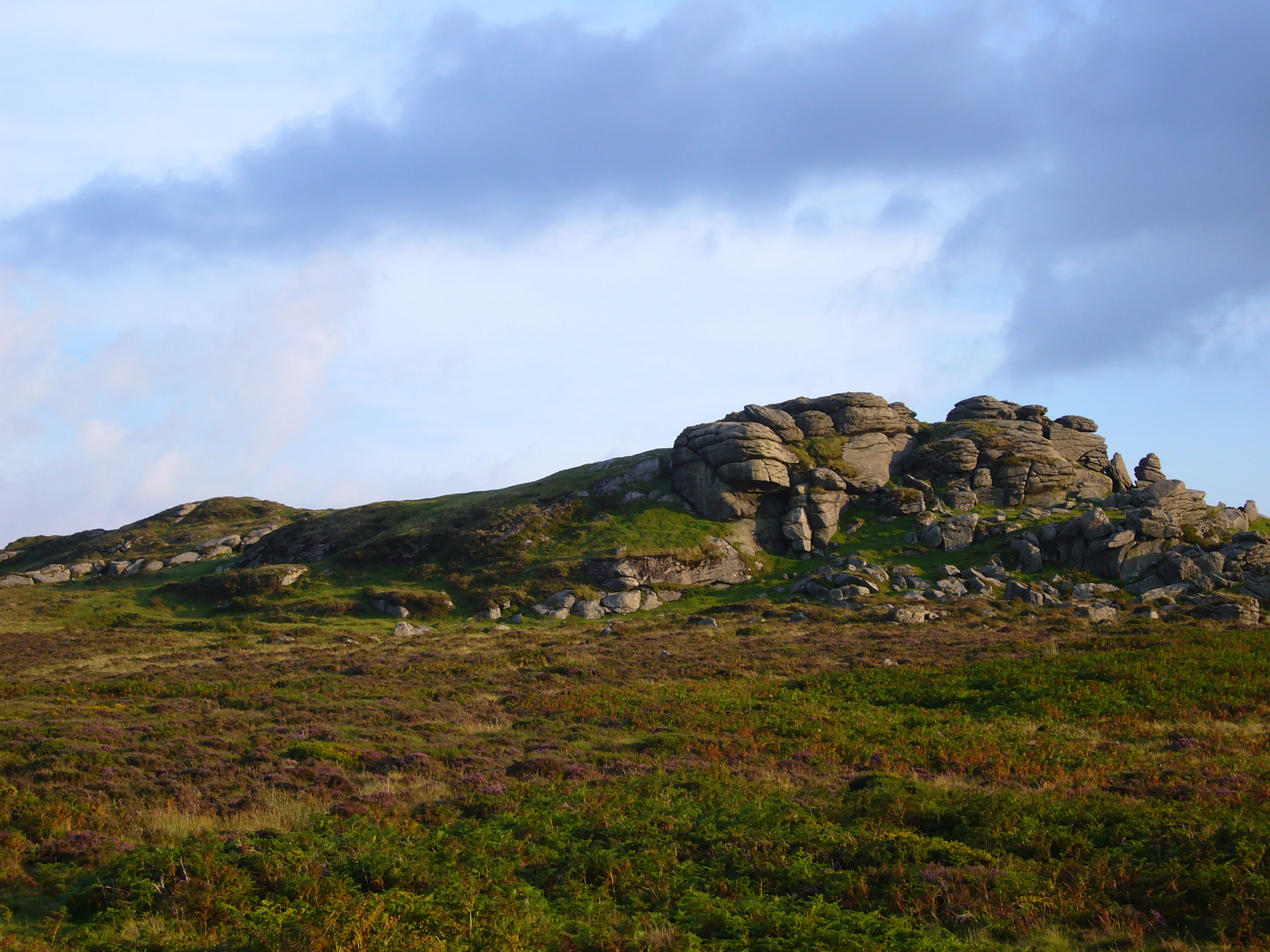 Rocky tor formations on moorland under a partly cloudy sky with scattered vegetation