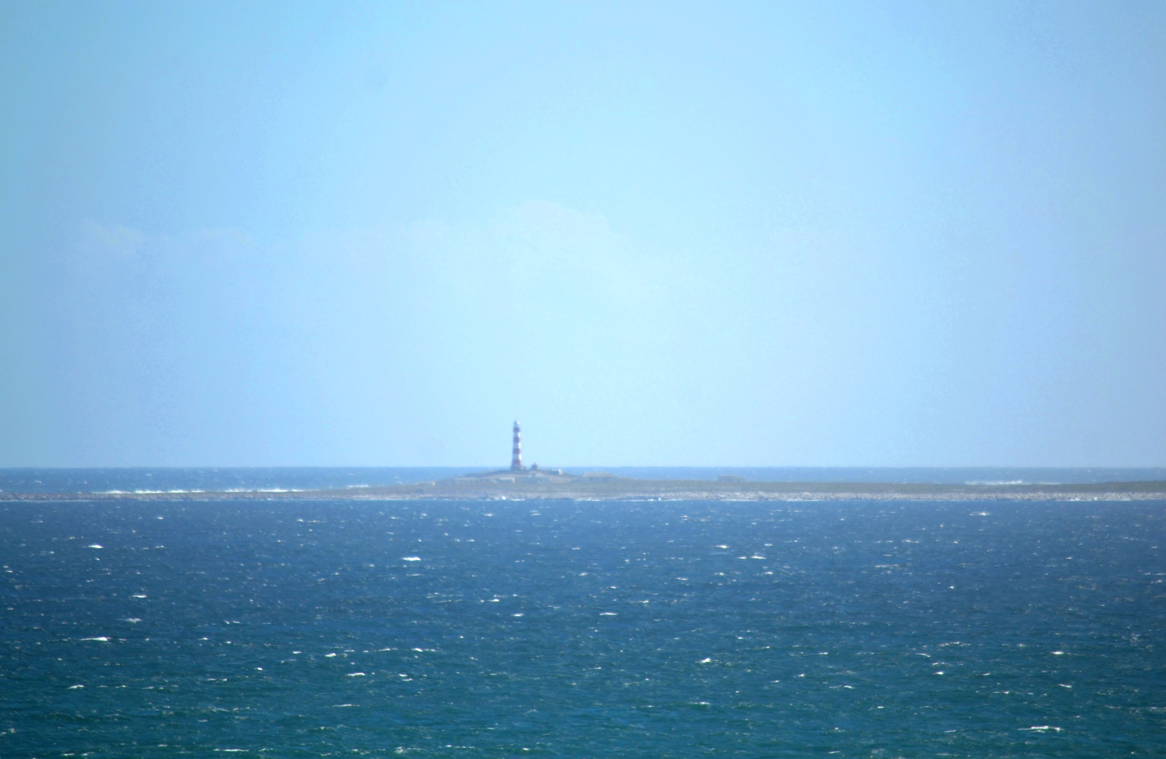 A distant view across the ocean showing Dassen Island with its prominent lighthouse standing as a small vertical structure on the low-lying land.