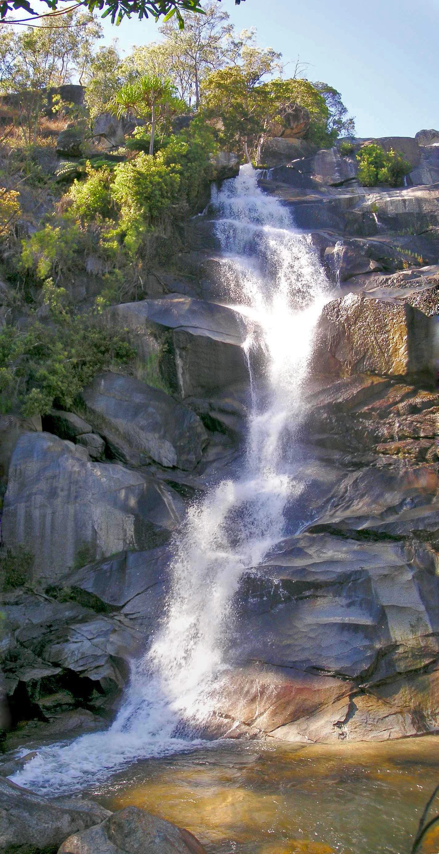 Waterfall flowing over rocky cliffs with lush green vegetation under clear blue sky