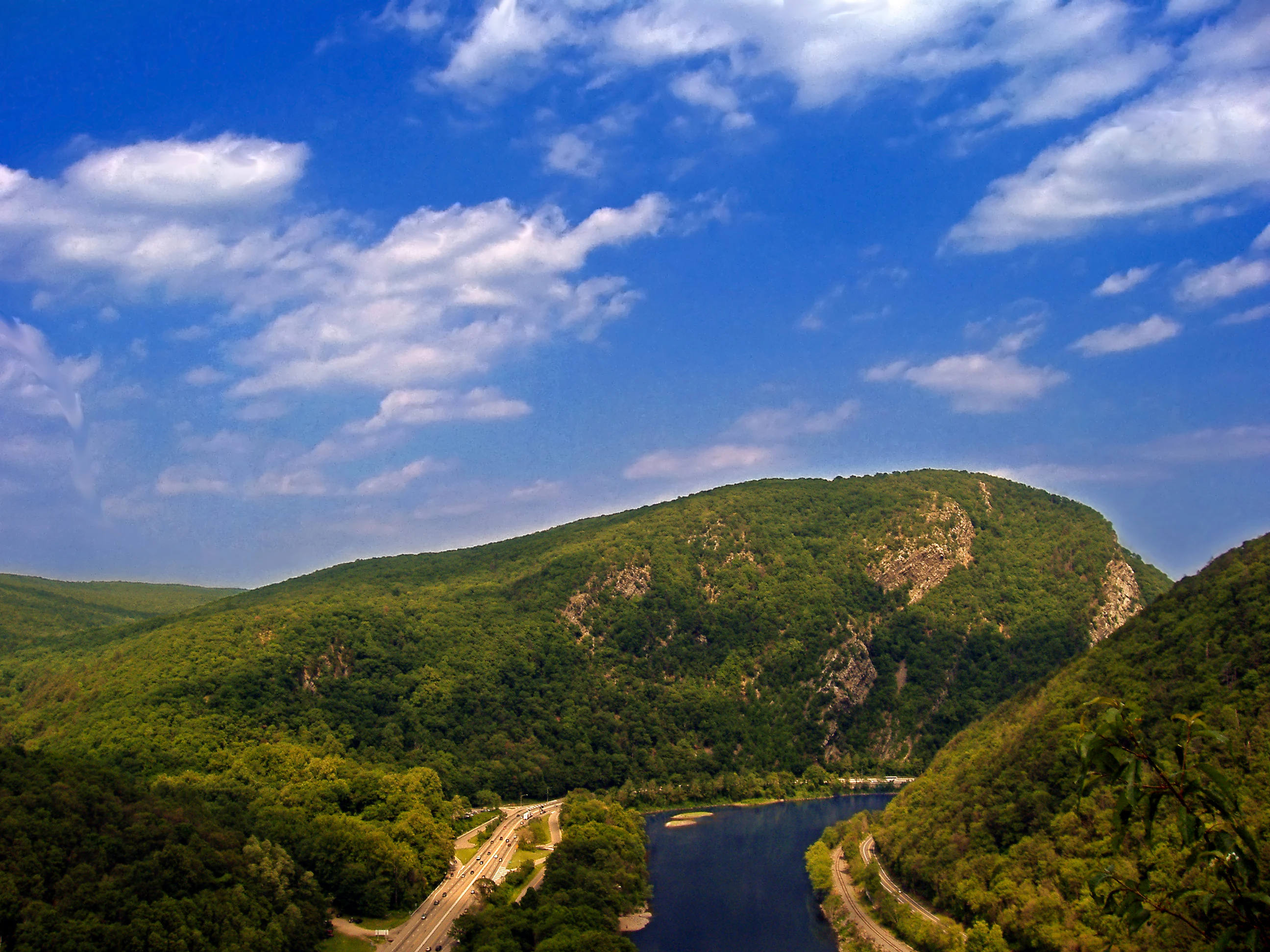 A high-angle view showing the Delaware River flowing through a deep, forested mountain pass with a road running alongside the river.