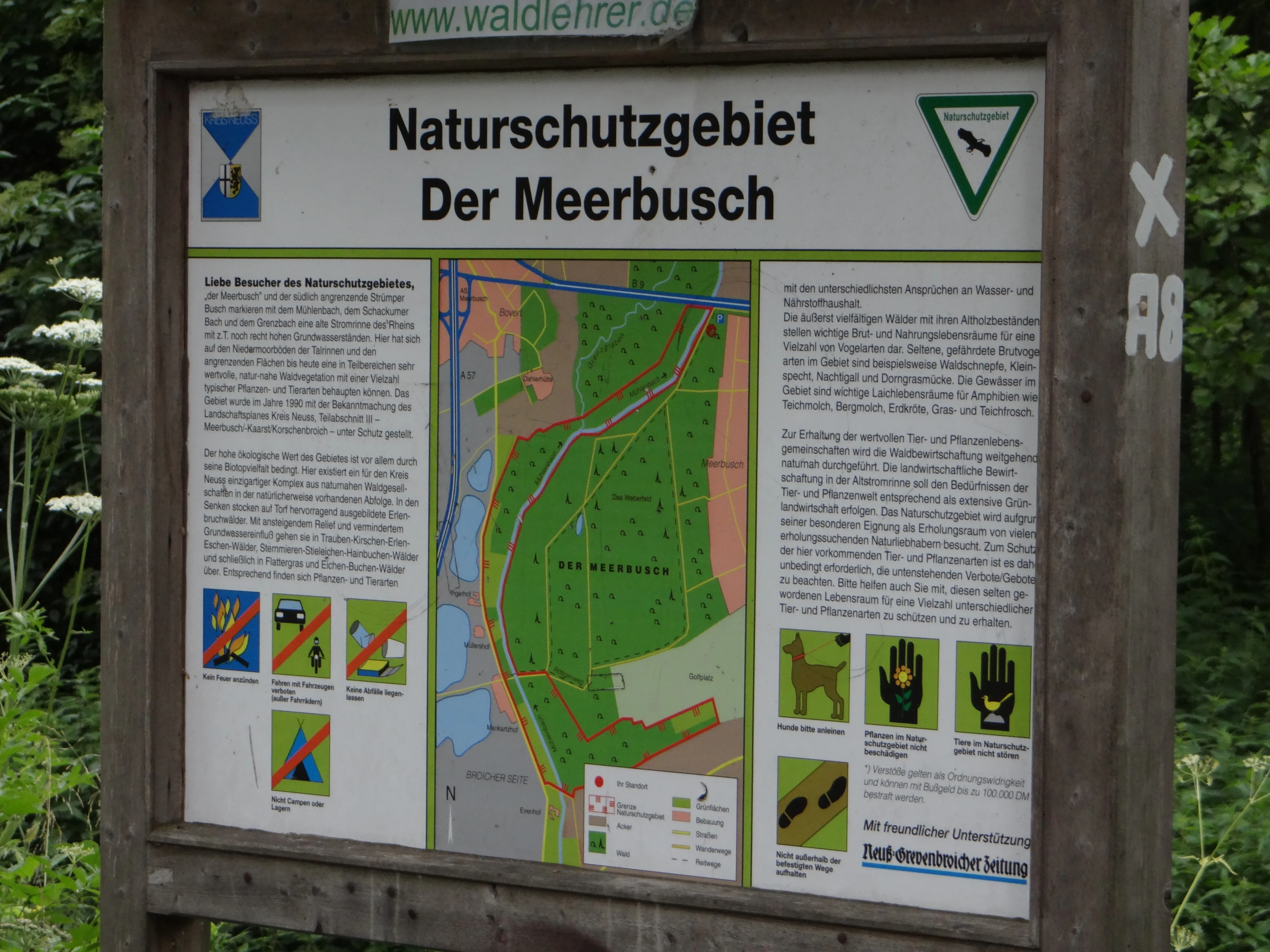 A wooden-framed information sign for the Der Meerbusch nature reserve, displaying a map and conservation rules.