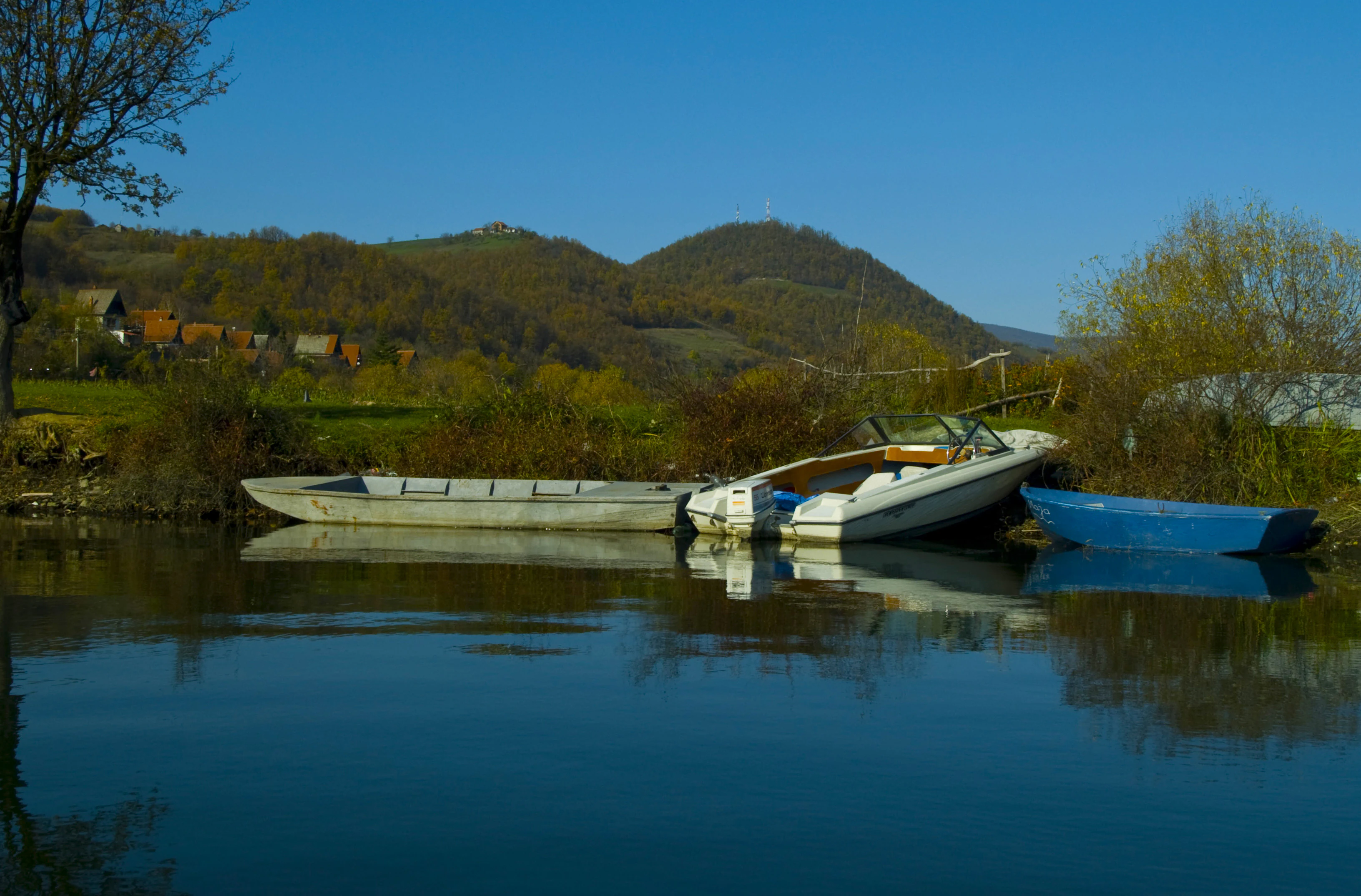 Several boats docked on calm water with hills and vegetation in the background under a clear blue sky