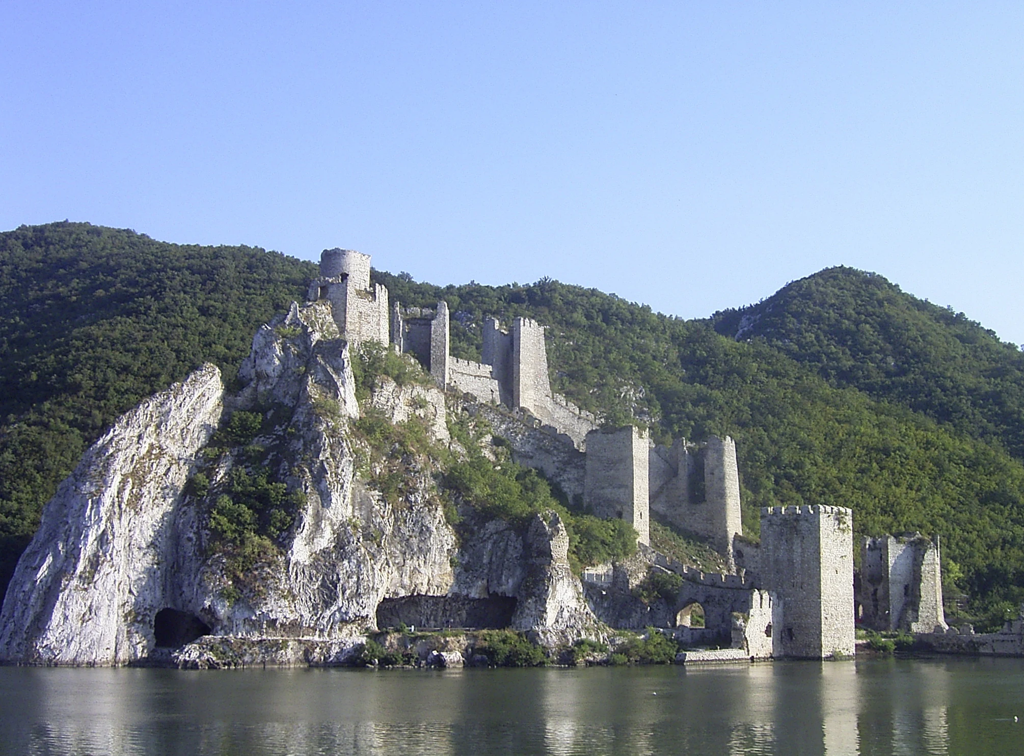 Medieval stone fortress on a rocky cliff overlooking a river with green hills in the background