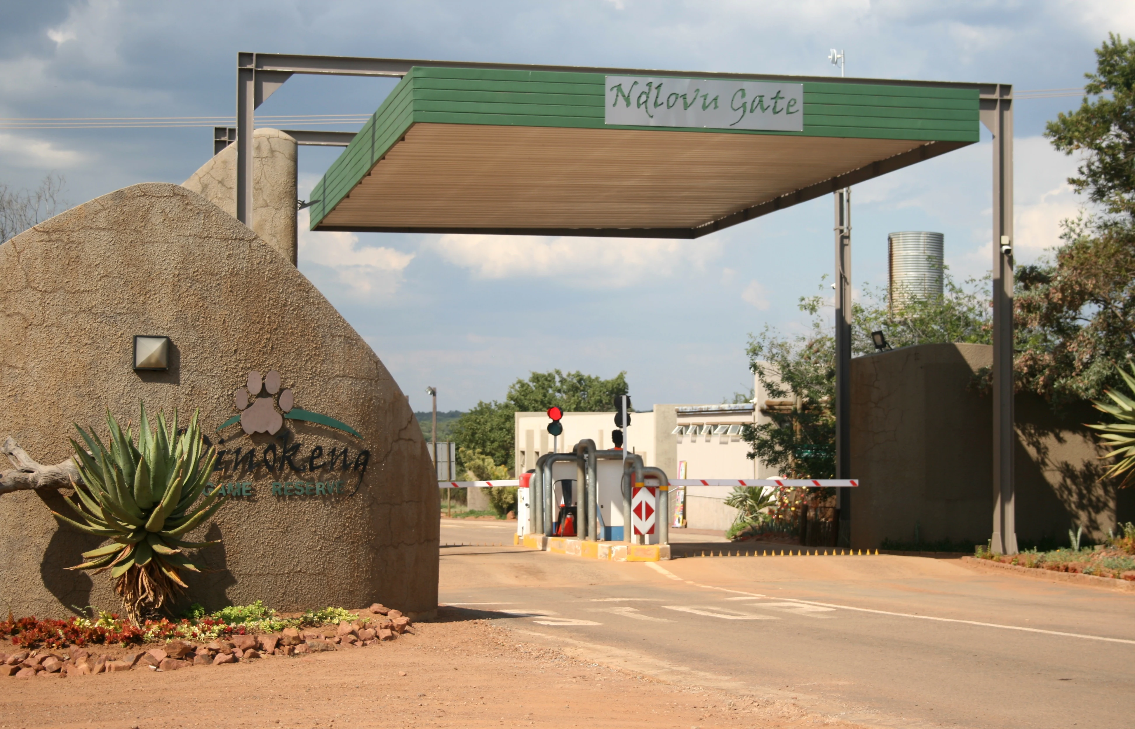 An entrance gate structure labeled Ndlovu Gate with a paved road leading into the Dinokeng Game Reserve, surrounded by stone pillars and vegetation.