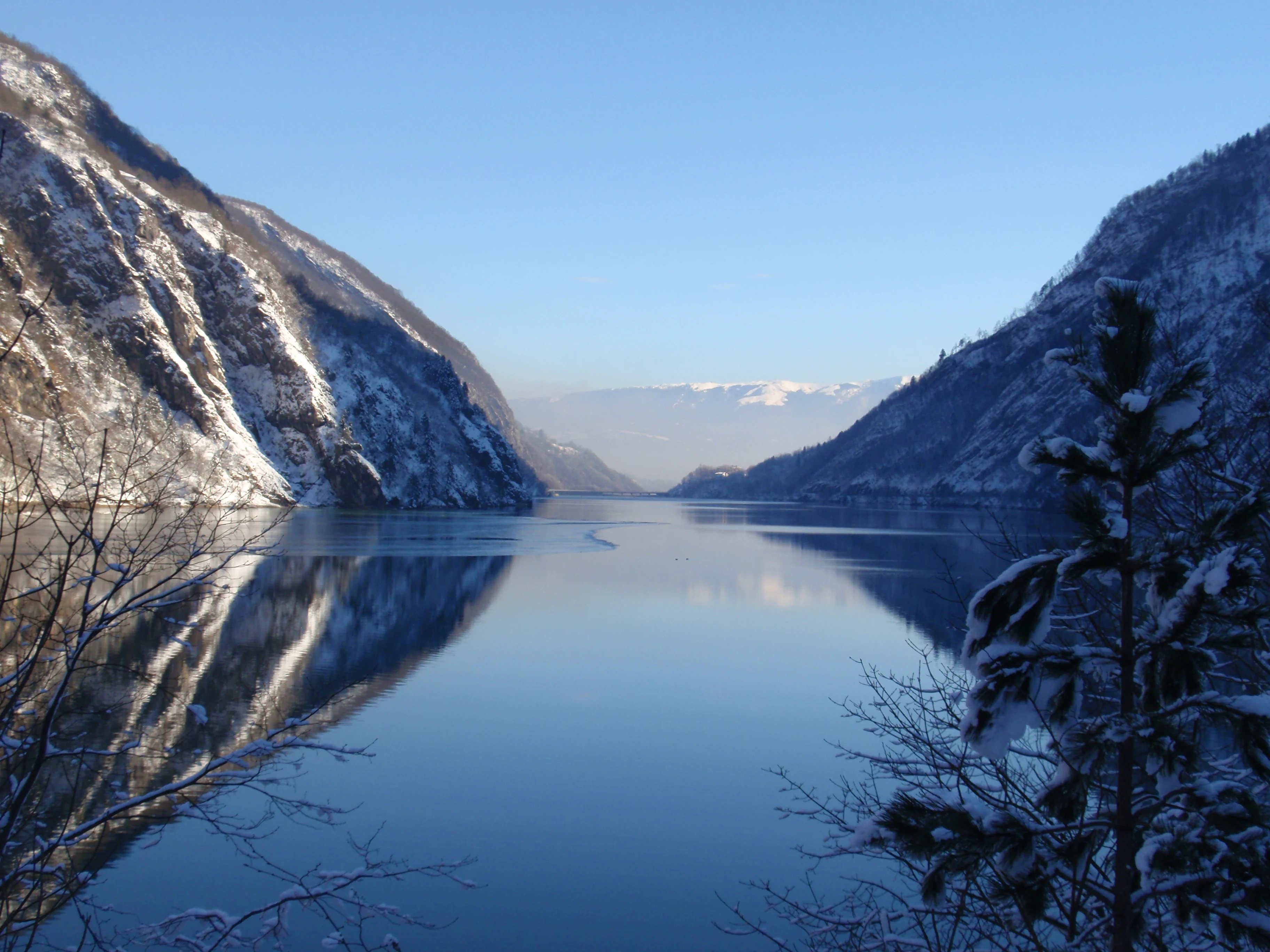 Snow-covered mountains reflect in a calm lake under a clear blue sky