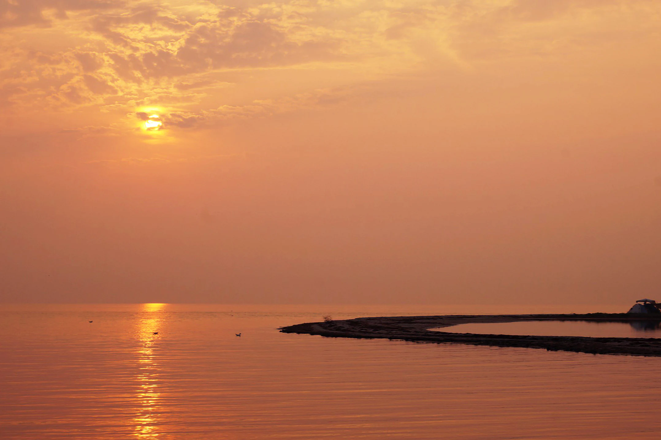 Sunset over calm sea waters with a small landmass and boat visible on the horizon