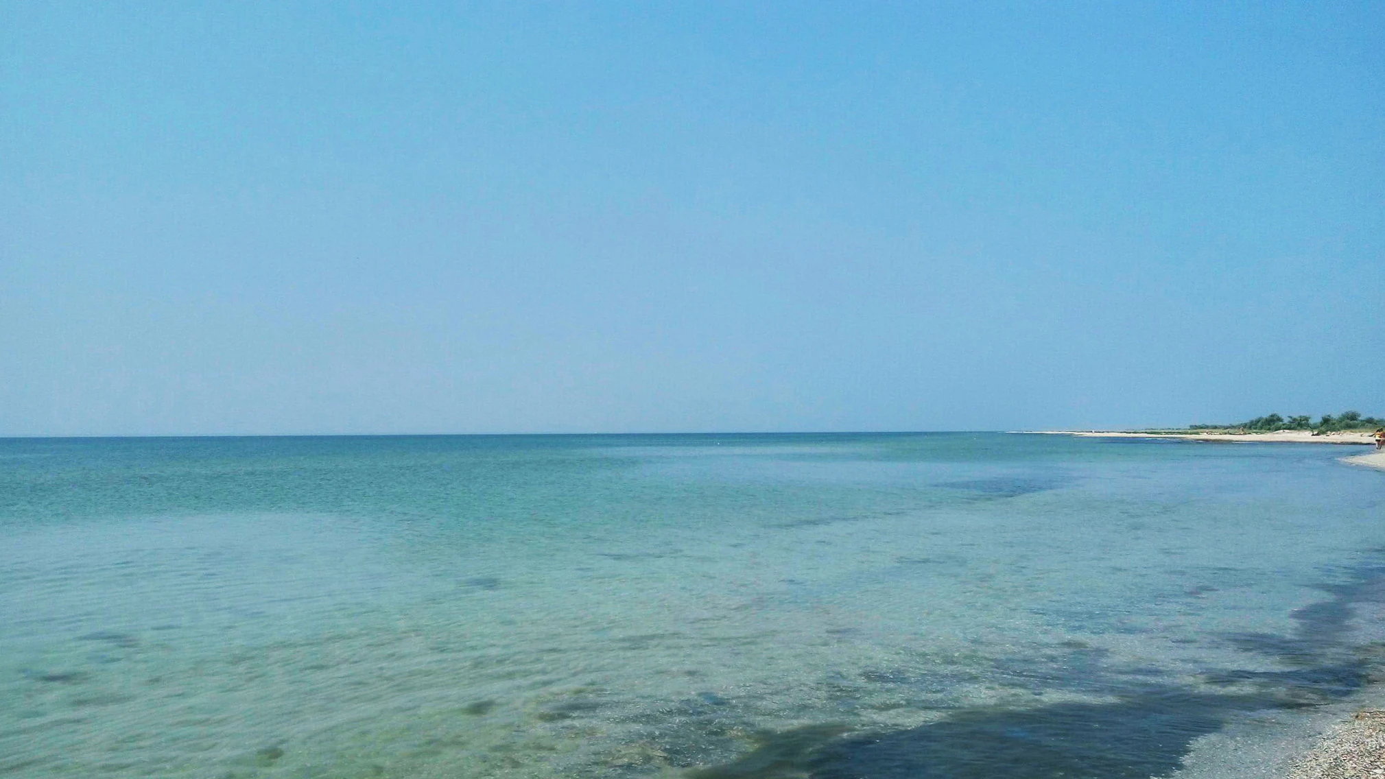 Clear blue sky over calm turquoise sea meeting sandy beach with shallow coastal waters