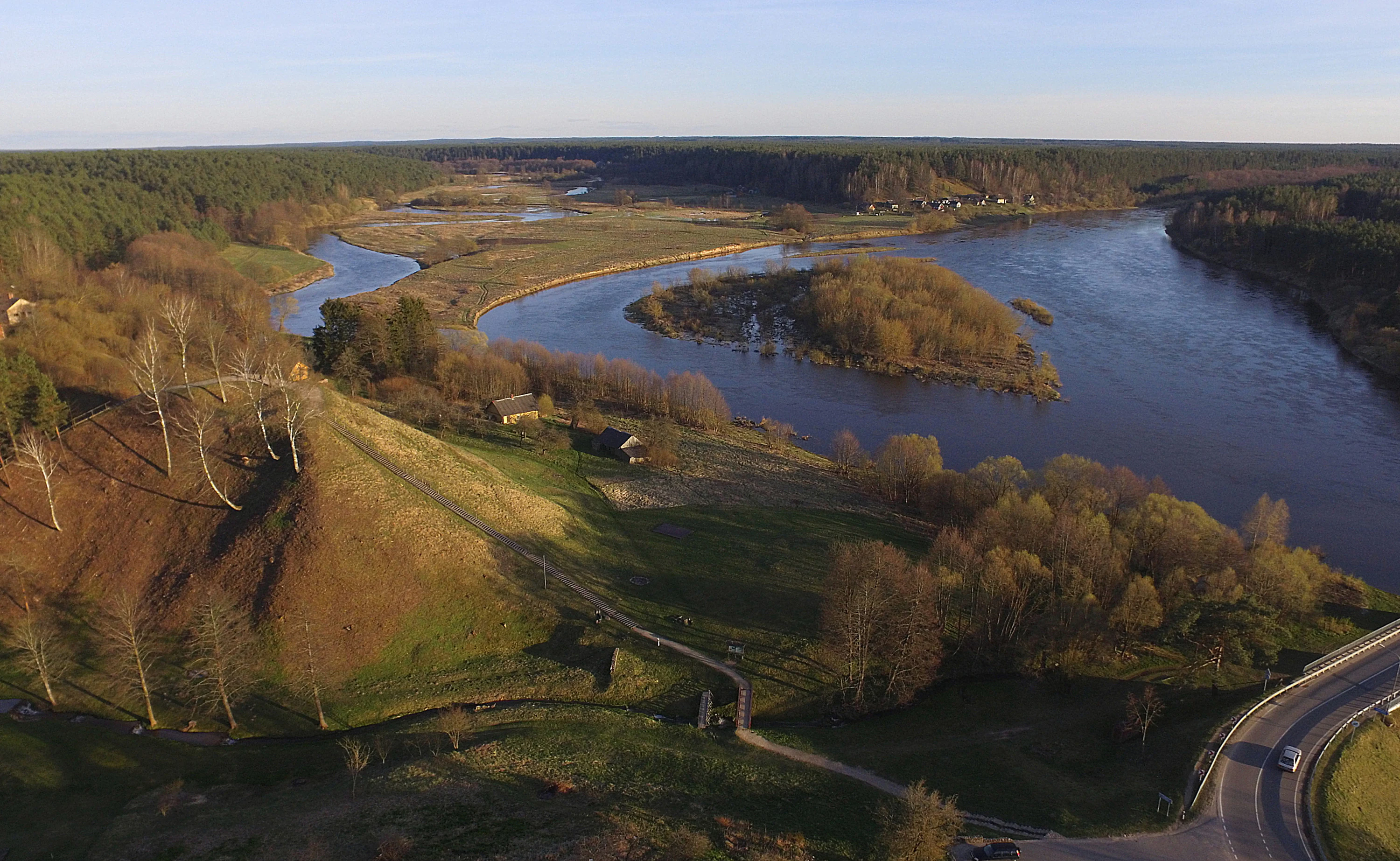 Aerial view of two rivers converging, a hillfort on a grassy hill, surrounded by forests and open fields