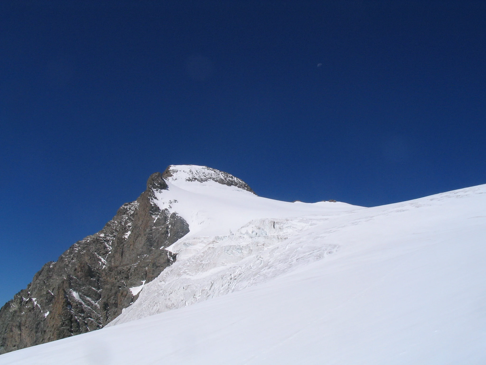 Snow-covered mountain peak with rocky slopes under clear blue sky