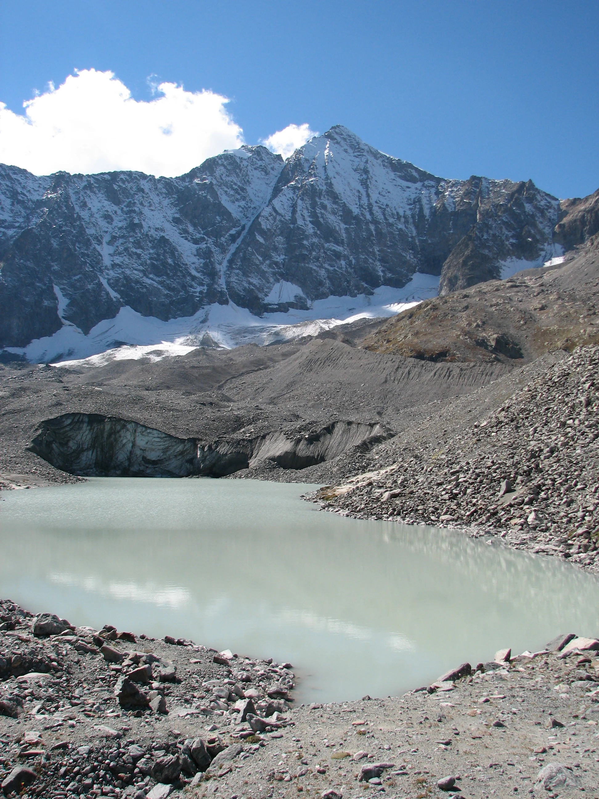 A glacial lake surrounded by rocky terrain with a glacier and snow-capped mountains under a clear blue sky
