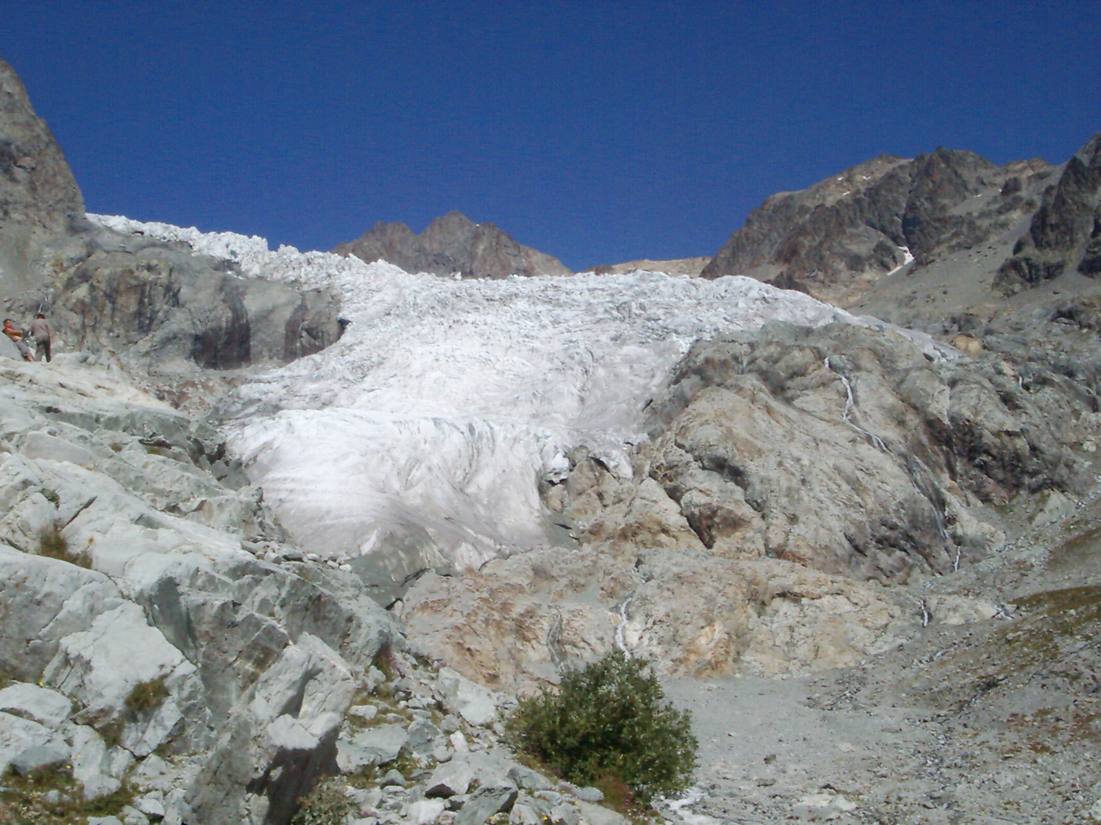 Wide view of Glacier Blanc, a large ice formation surrounded by rocky mountains under a clear blue sky.