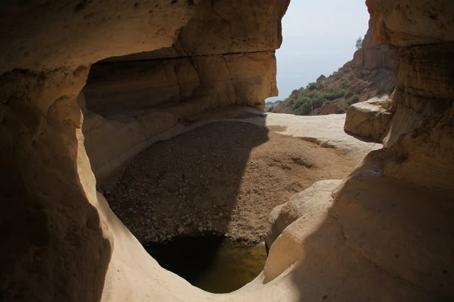 Rock arch formation framing a small water pool in a desert landscape