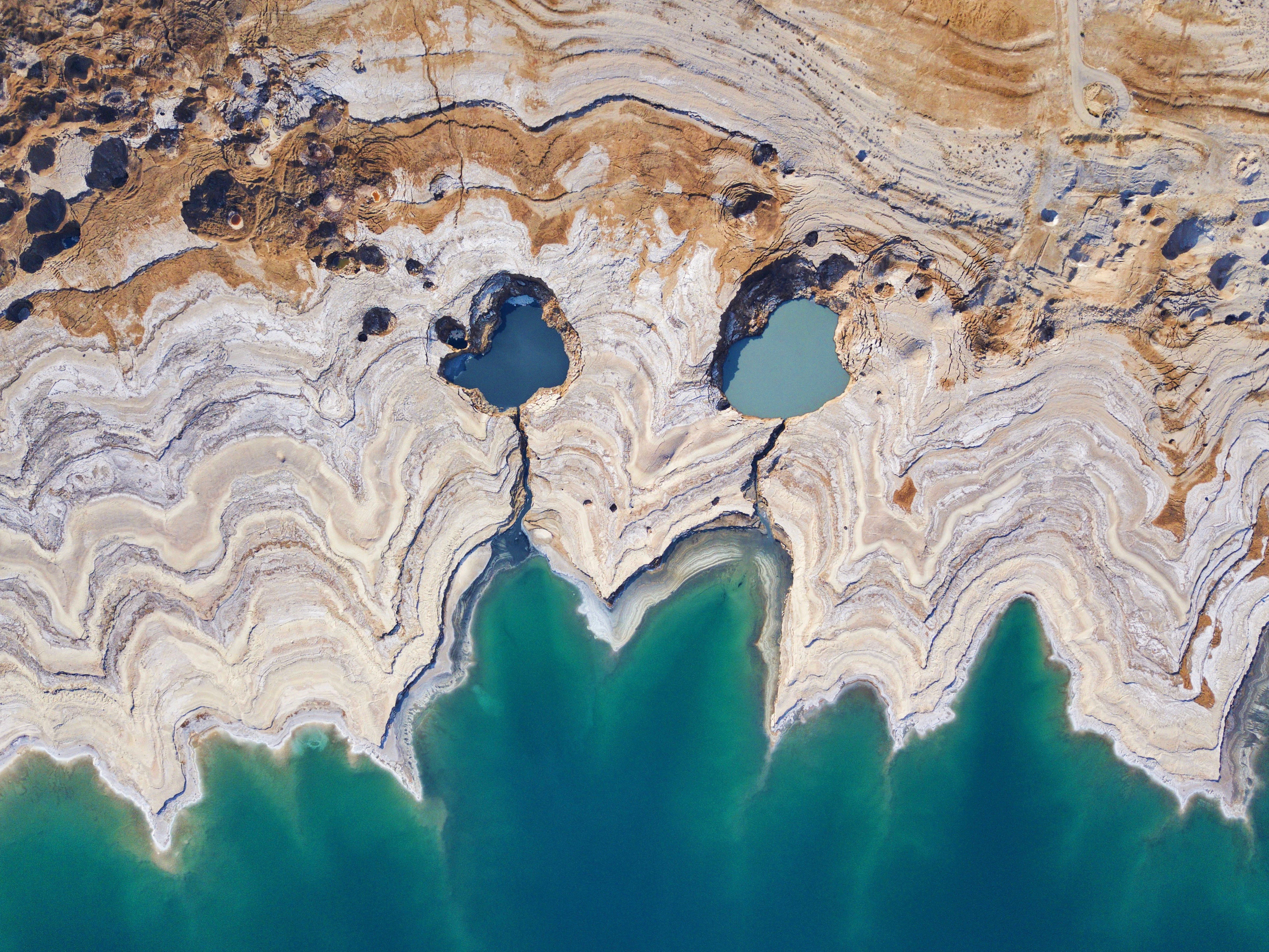 Aerial view showing two distinct sinkholes filled with water, surrounded by layered rock formations and a body of water