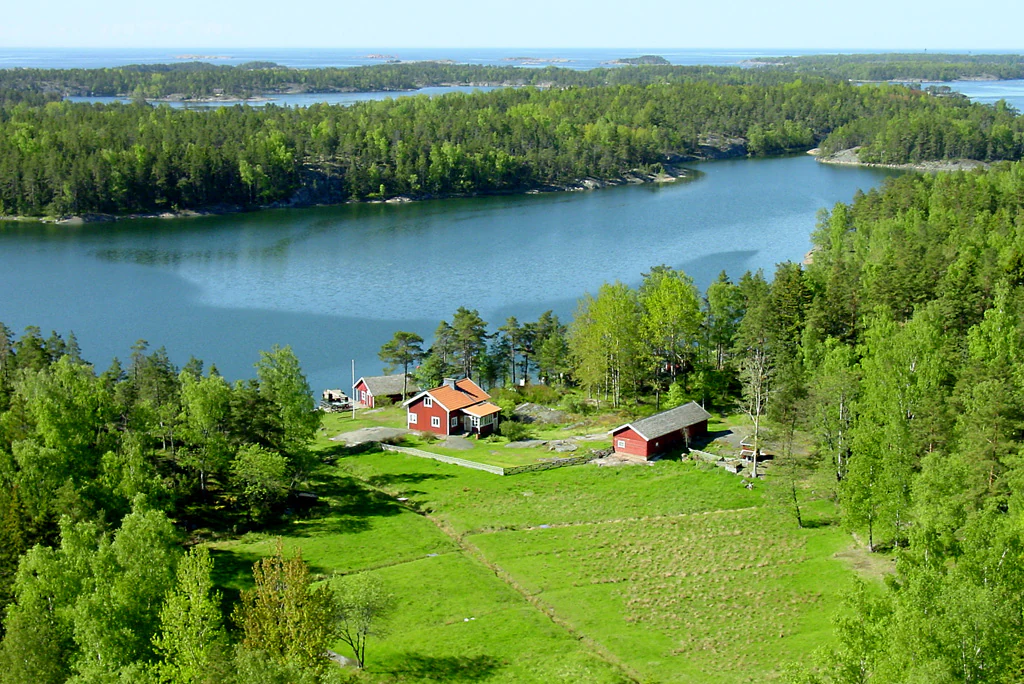 Aerial view showing red farm buildings, green fields, and surrounding water with forested islands in the background