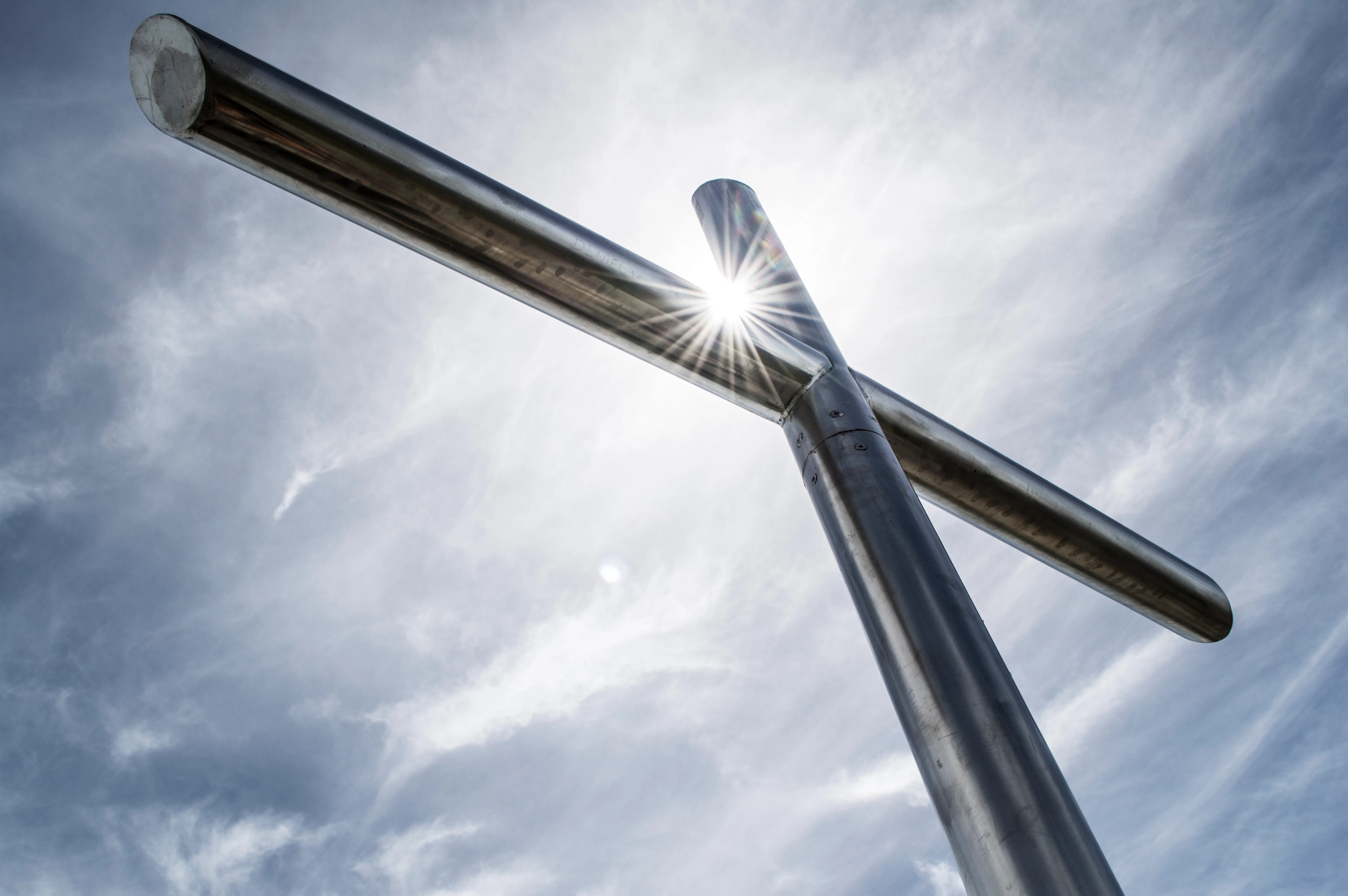 Metal cross structure with sun flare against a cloudy sky
