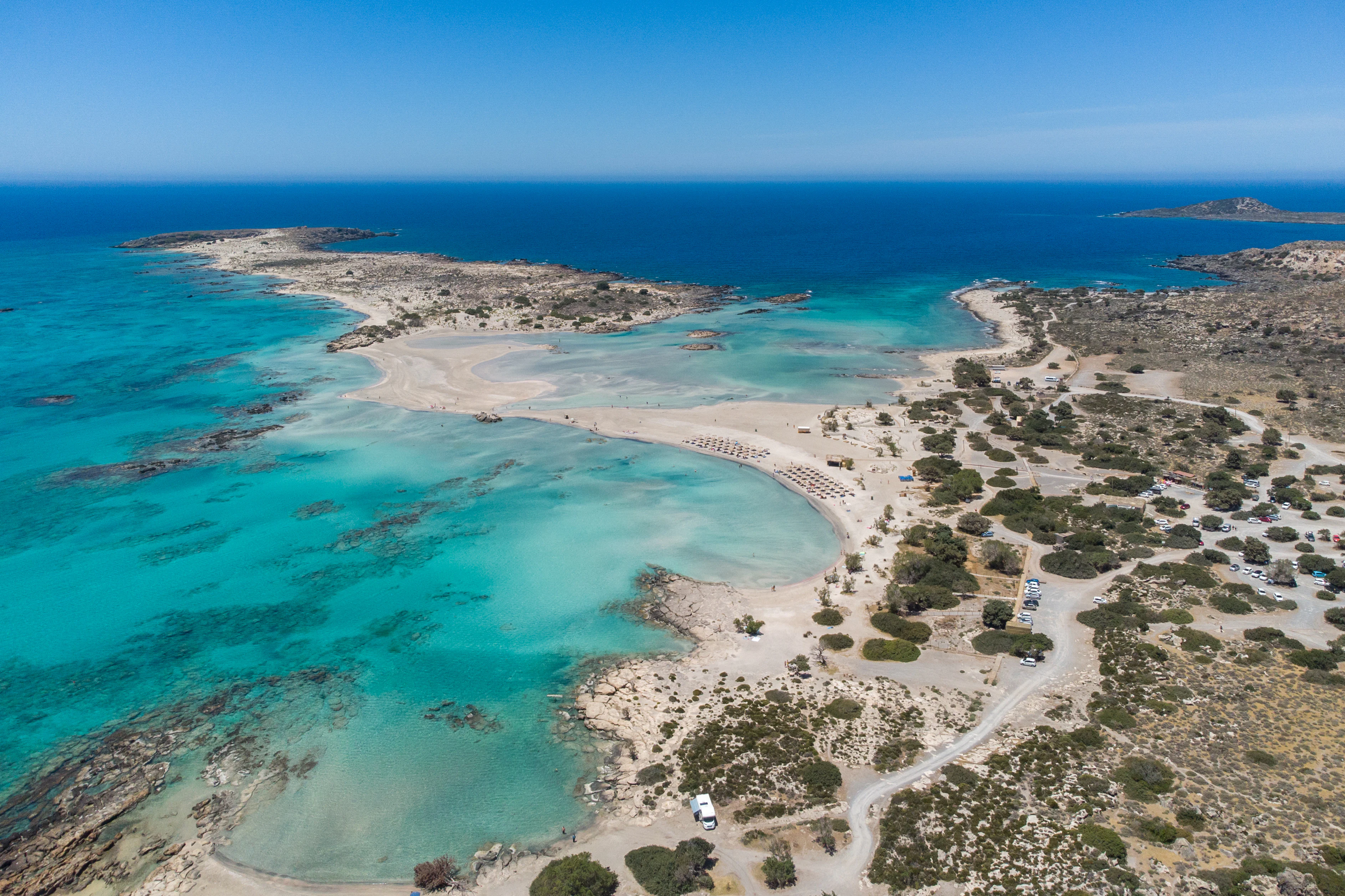 Aerial perspective looking over the turquoise shallow waters, sandbanks, and rugged scrubland of Elafonisi beach in Crete.