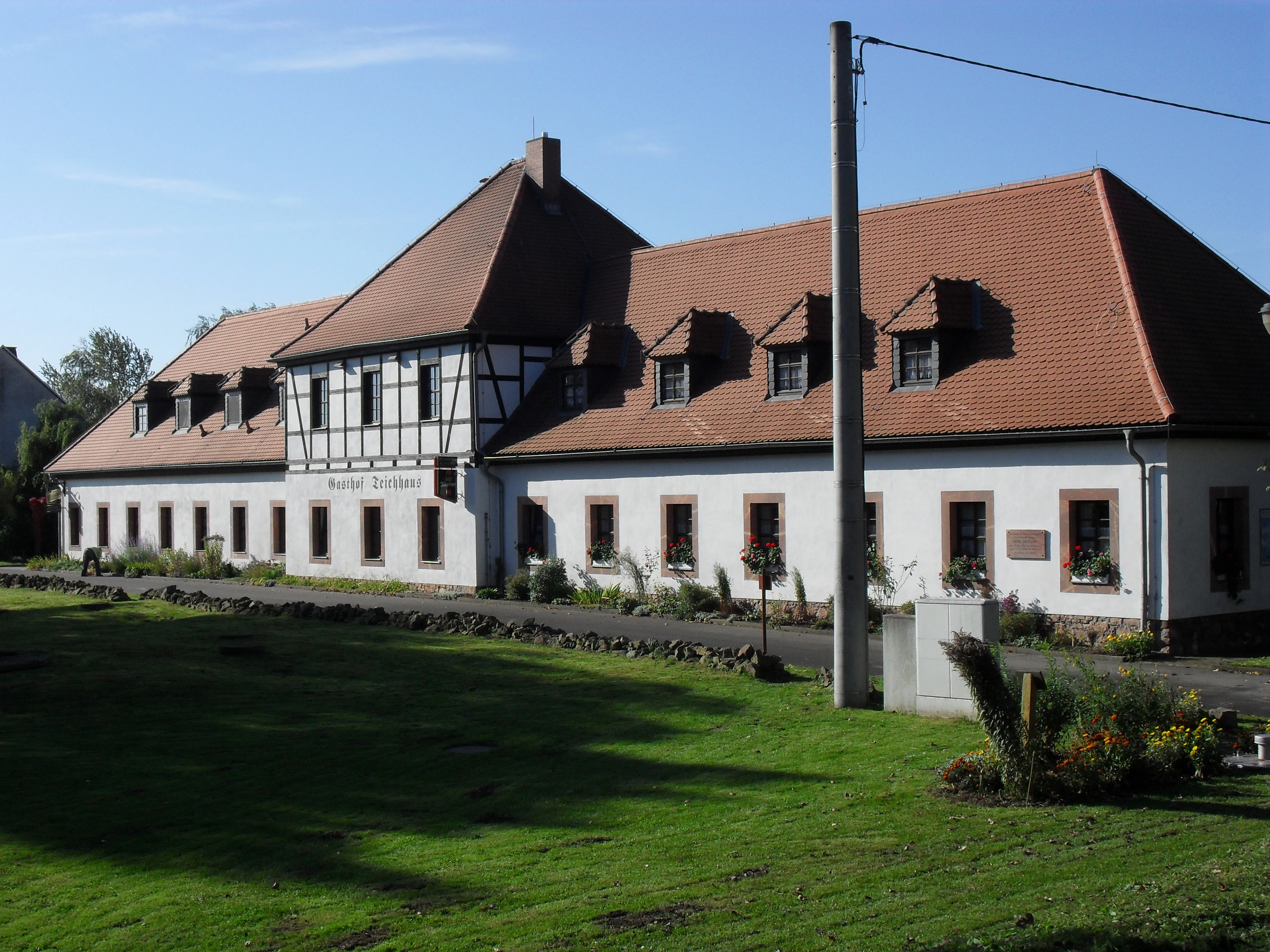 A long, traditional white building with half-timbered accents and a red tiled roof, situated next to a grassy area.