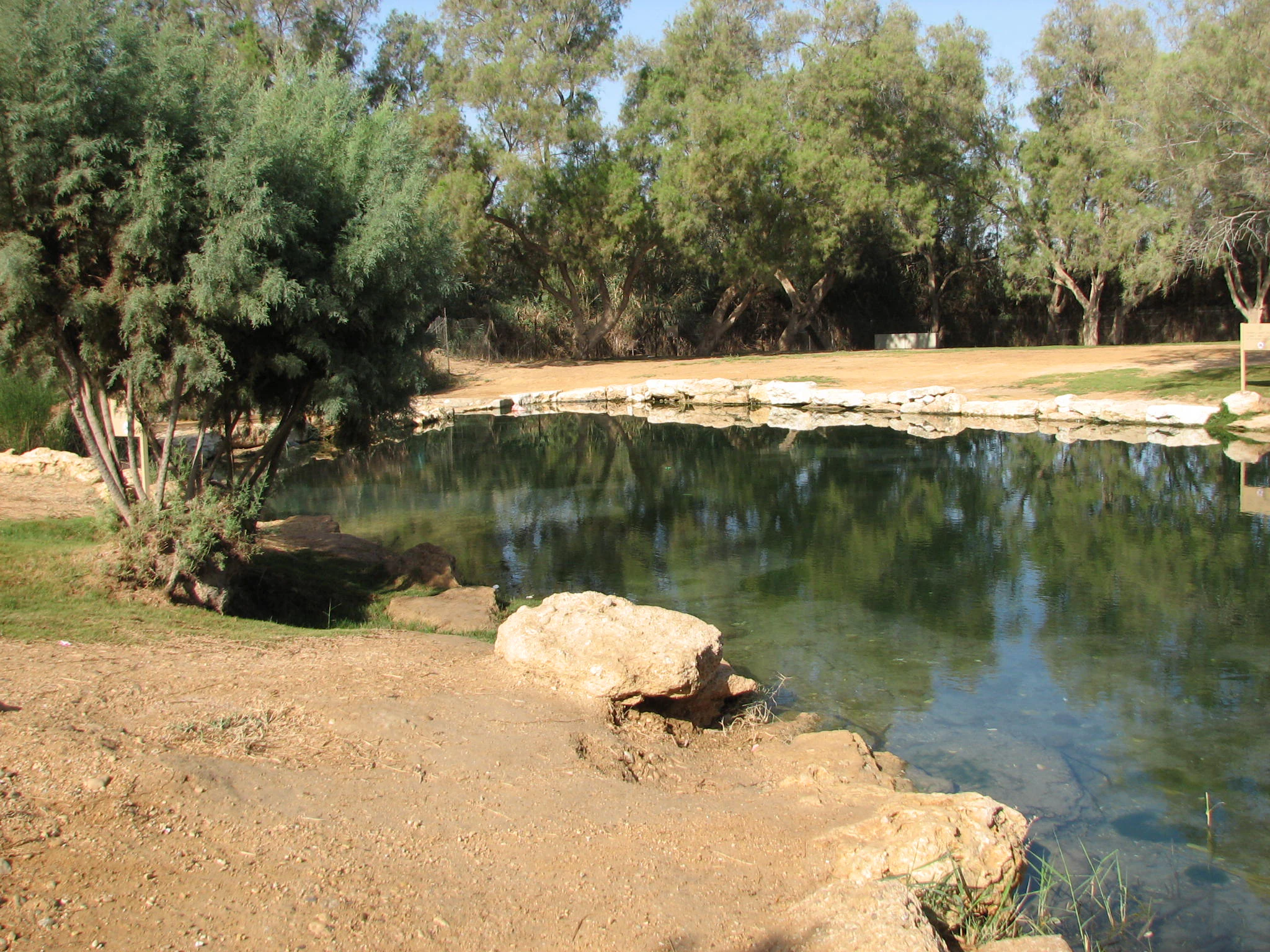Natural spring surrounded by trees and rocks with calm water reflecting sky and foliage