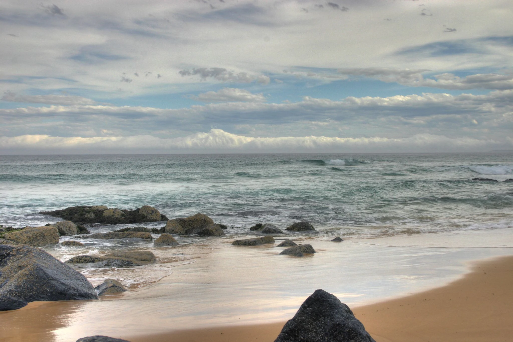 Sandy beach with rocky outcrops and ocean under partly cloudy sky