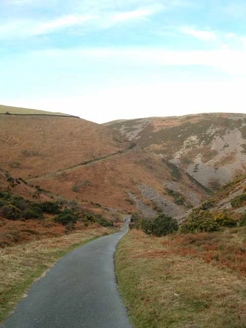 A paved road winding through a moorland valley with rolling hills and brown and green vegetation