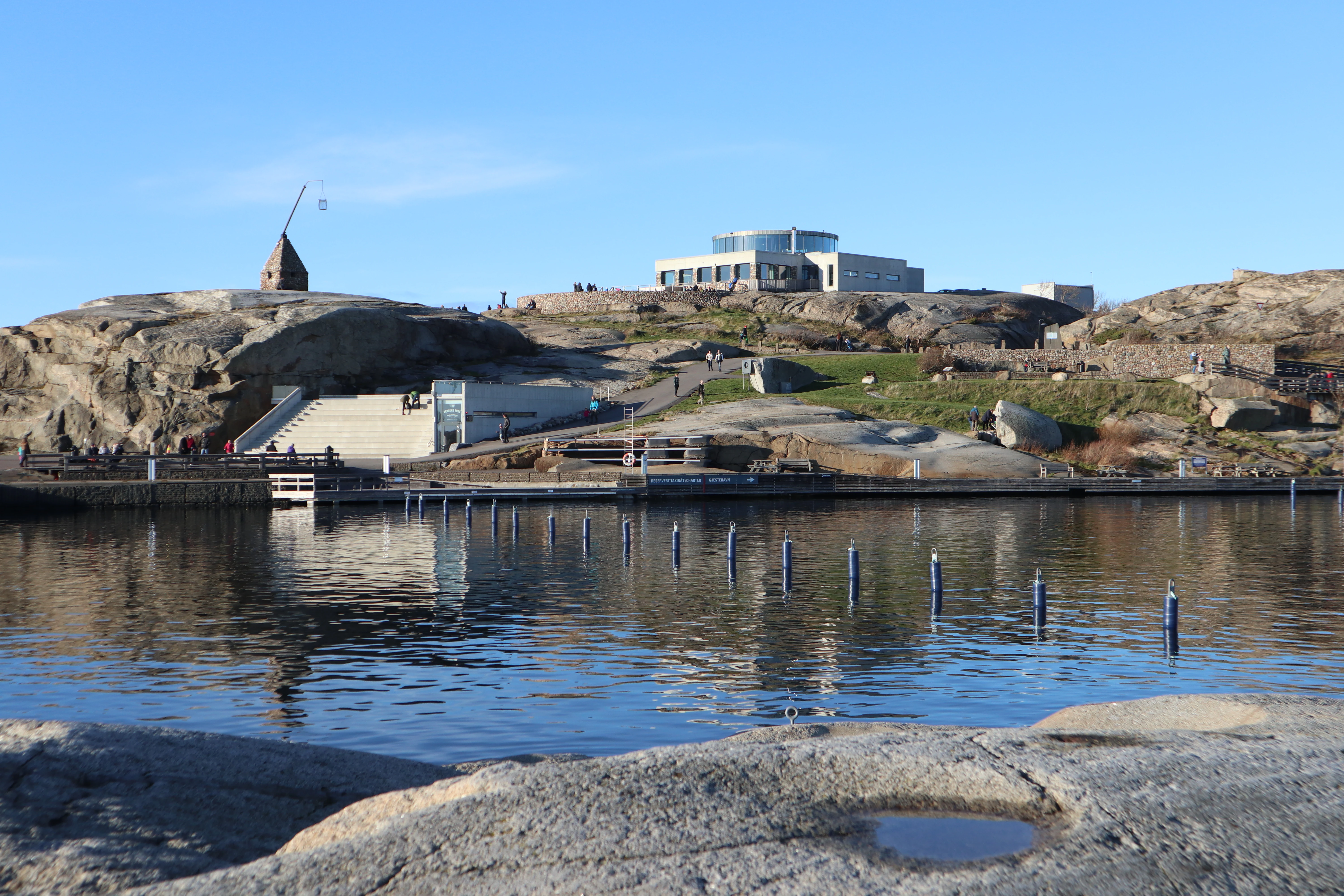 Waterfront view of a visitor center building on rocky terrain with calm water reflecting the structure