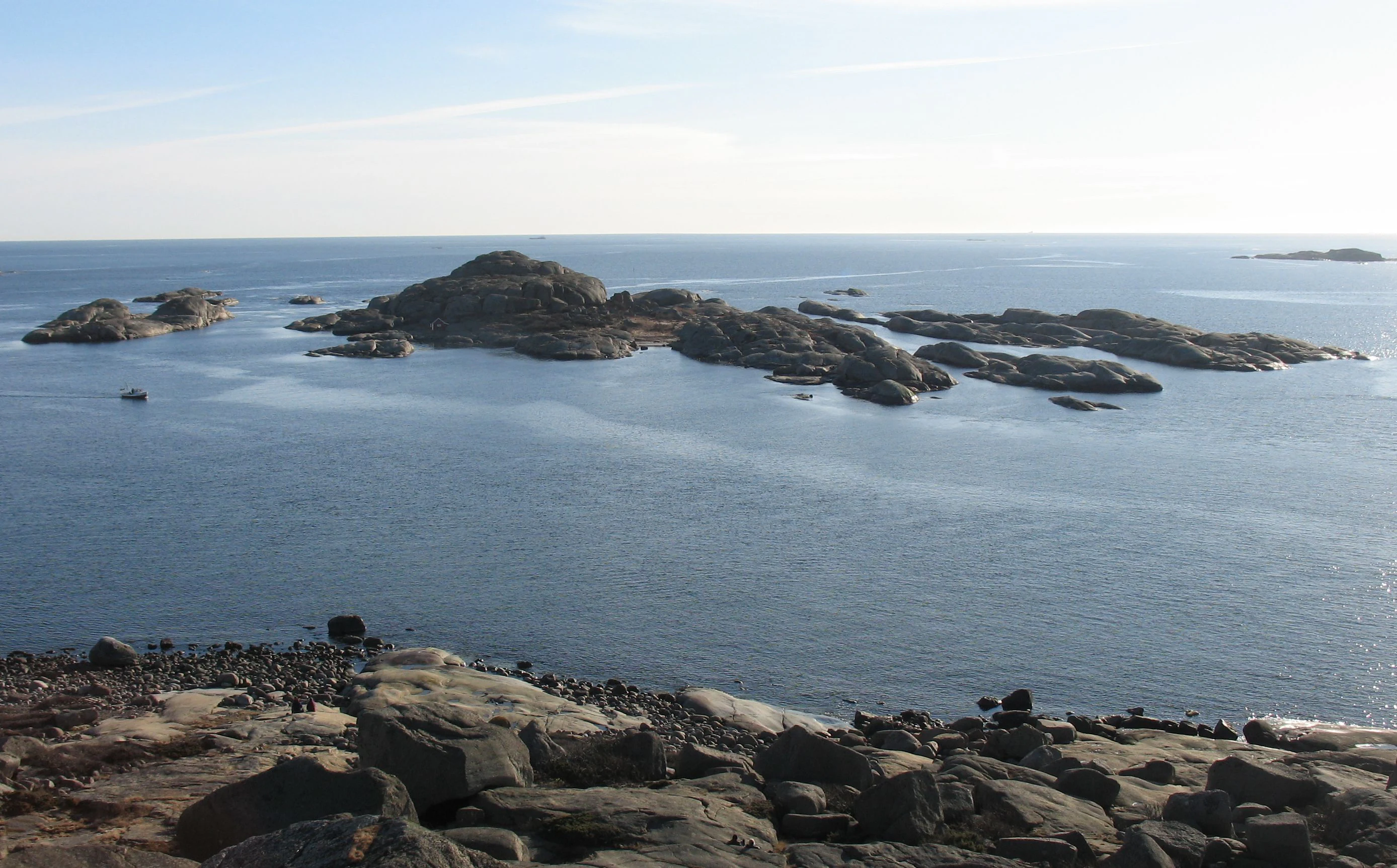 Rocky shoreline with multiple small islands in open water under clear sky