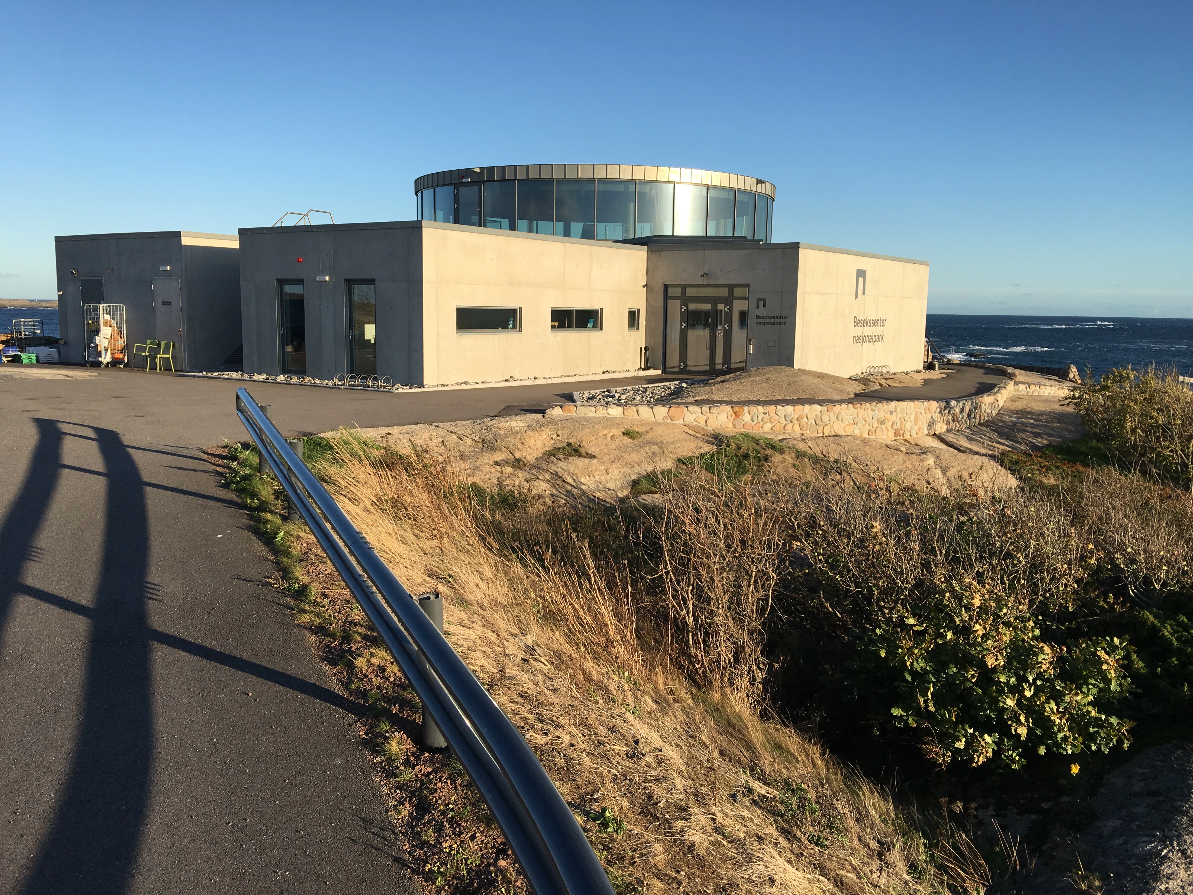 Visitors' center building with circular upper section on coastal cliff overlooking ocean, paved road with guardrail in foreground