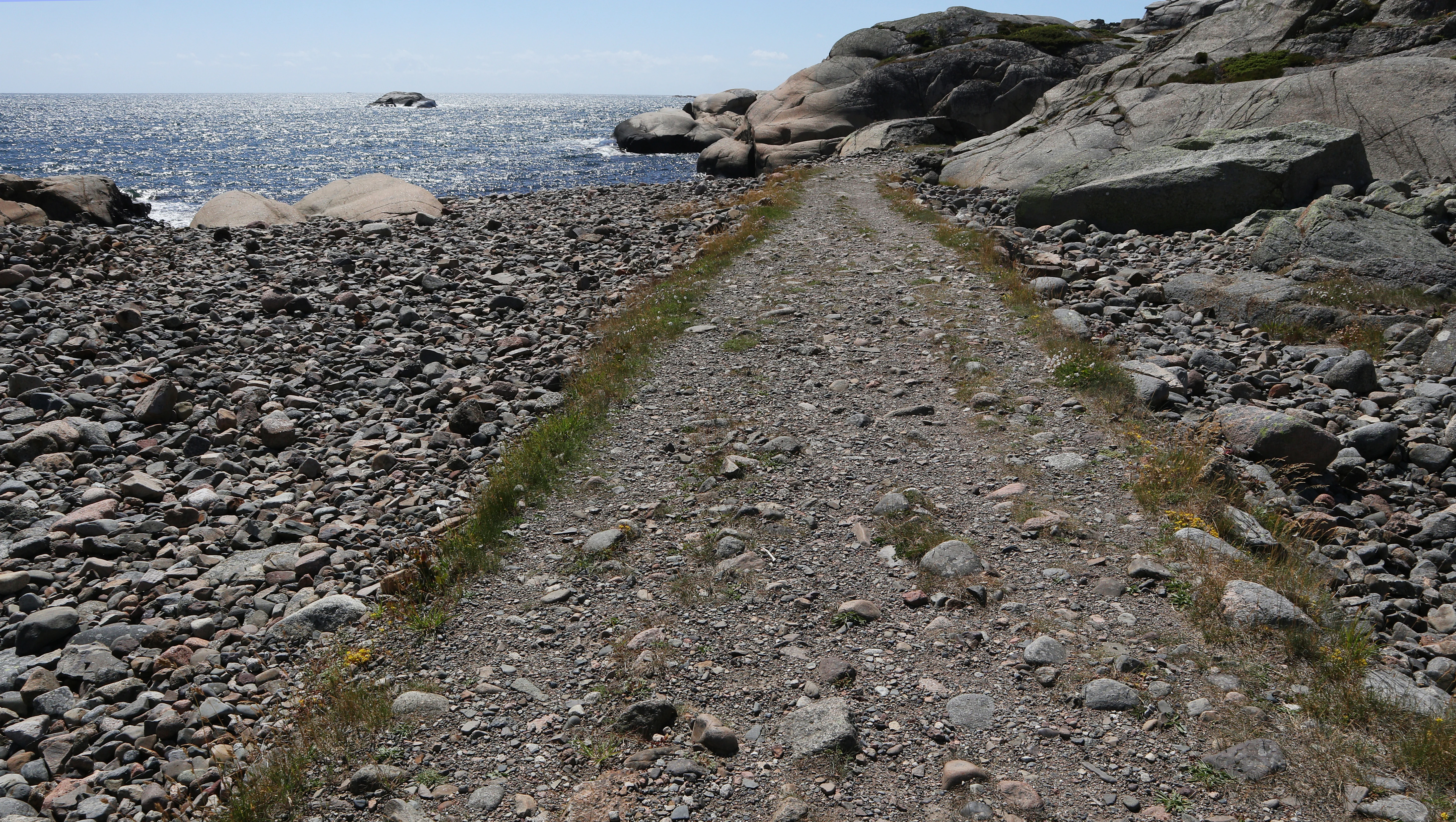 A gravel trail on a rocky shoreline with the ocean in the background