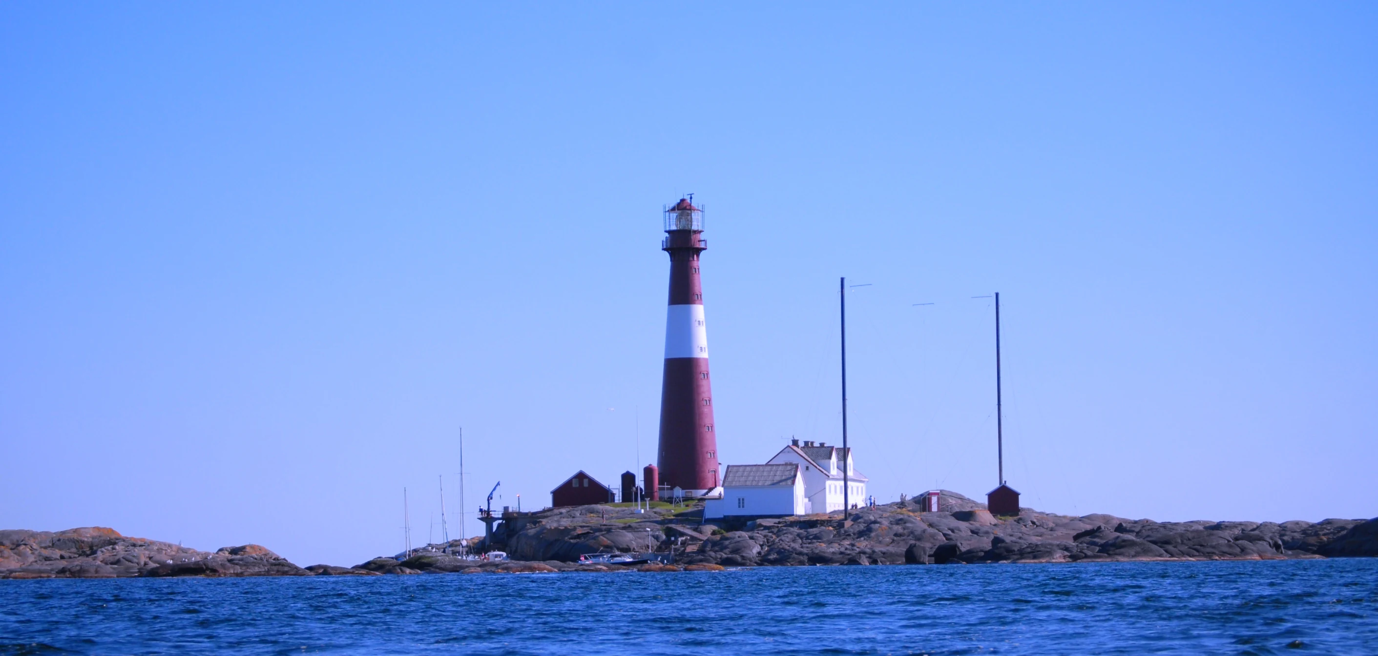 Red and white lighthouse on a rocky island surrounded by blue water under a clear blue sky
