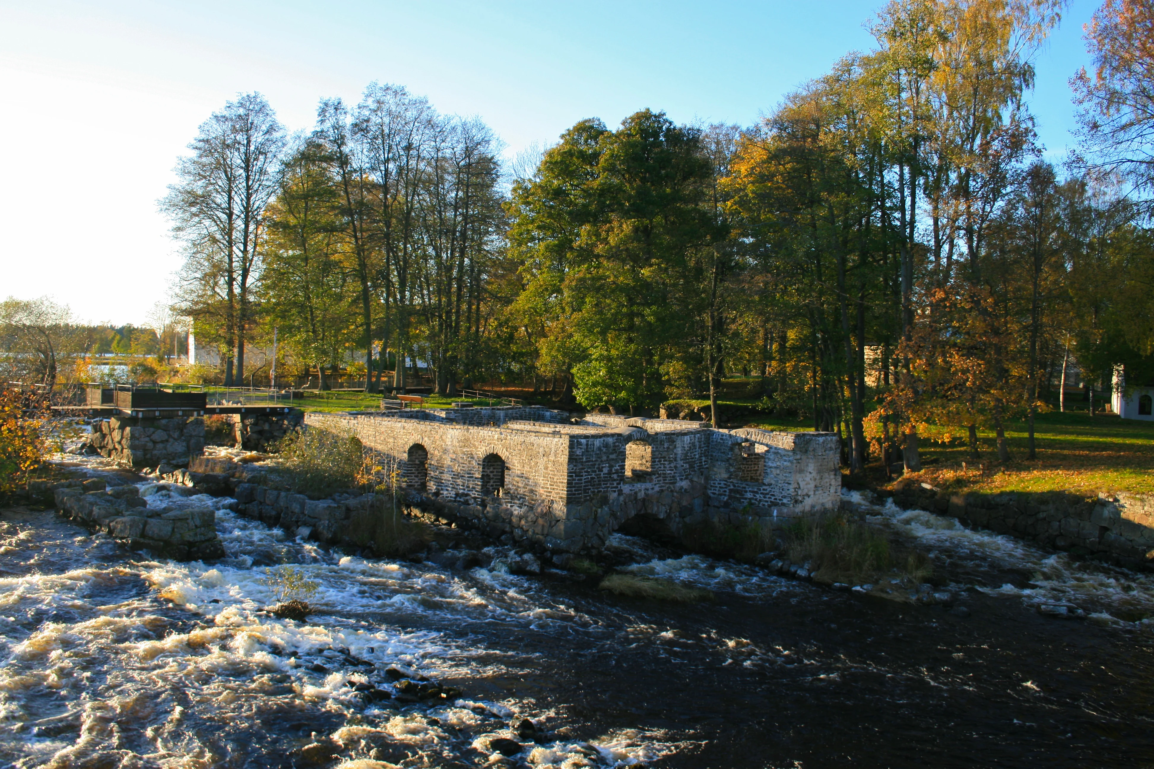 Stone structure of old mill on river with flowing water and trees in background