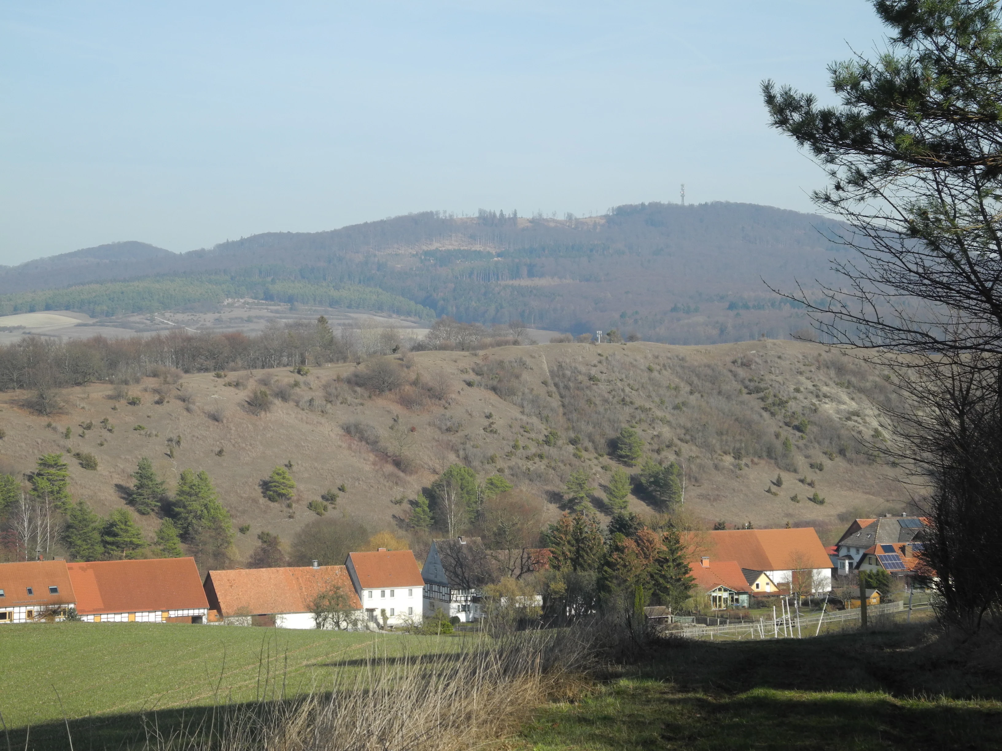 A wide landscape view of a hilly nature reserve with a rural village nestled in the foreground, under a clear sky.