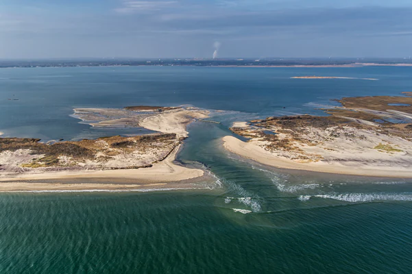 Aerial view of a breach in a sandy barrier island, showing water flowing from the open ocean into a sheltered bay.