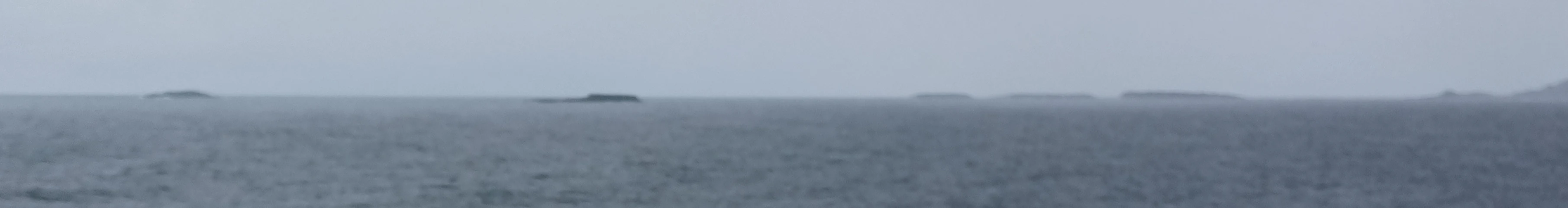 A wide, low-angle shot of several small islands on the horizon, separated by open water under a gray, overcast sky.