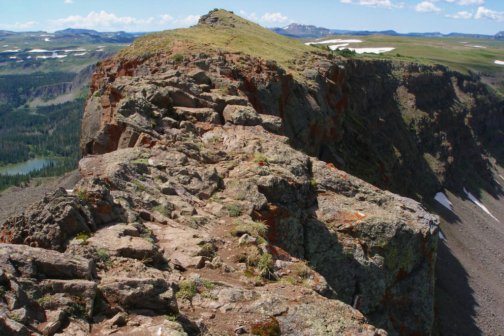 Una vista en ángulo alto a lo largo de una estrecha línea de cresta rocosa conocida como Devils Causeway, con acantilados escarpados que caen a ambos lados hacia laderas cubiertas de hierba y mesetas alpinas distantes.