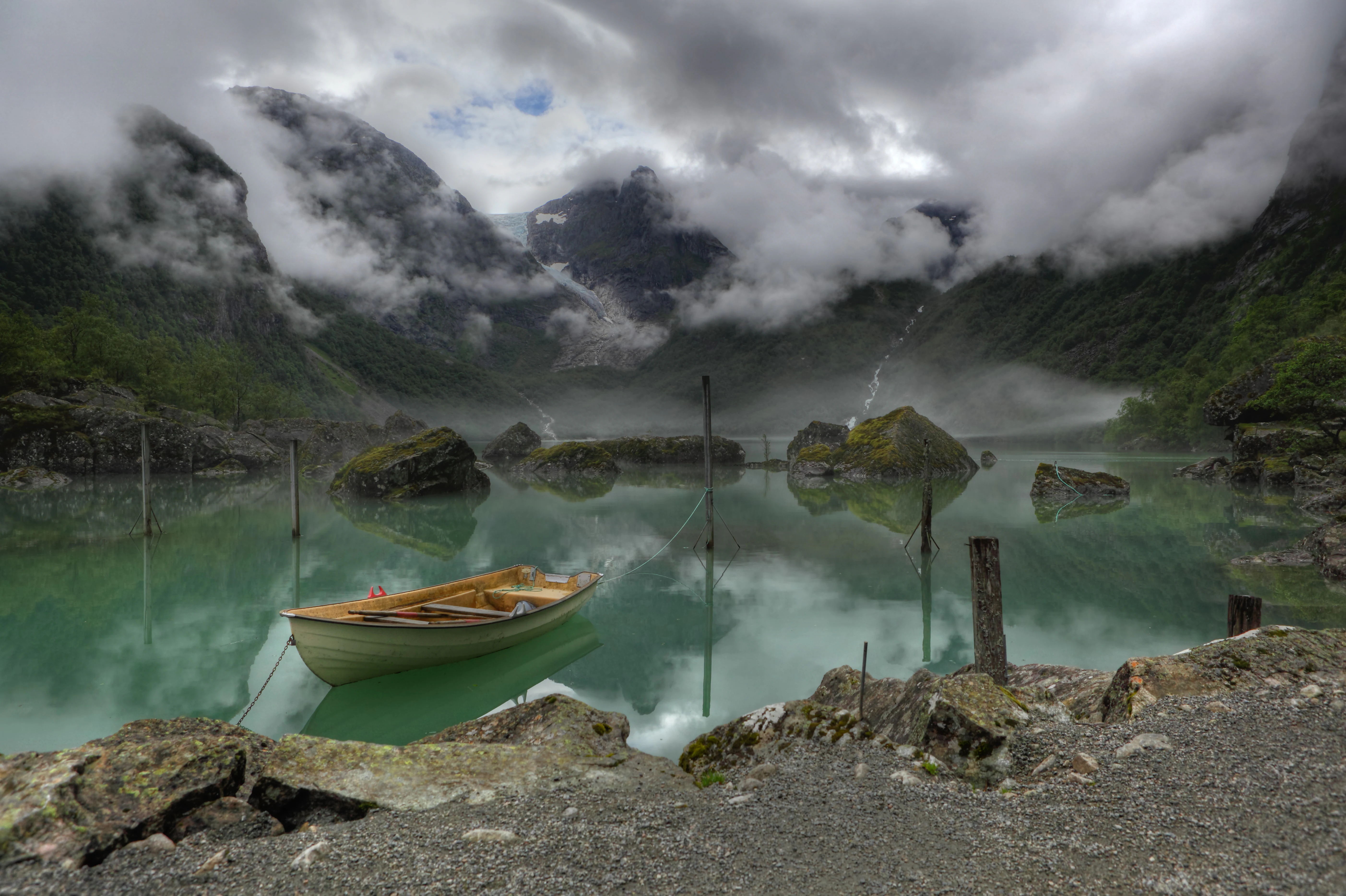 Yellow boat docked at rocky shore beside turquoise lake with mountains and glacier in background