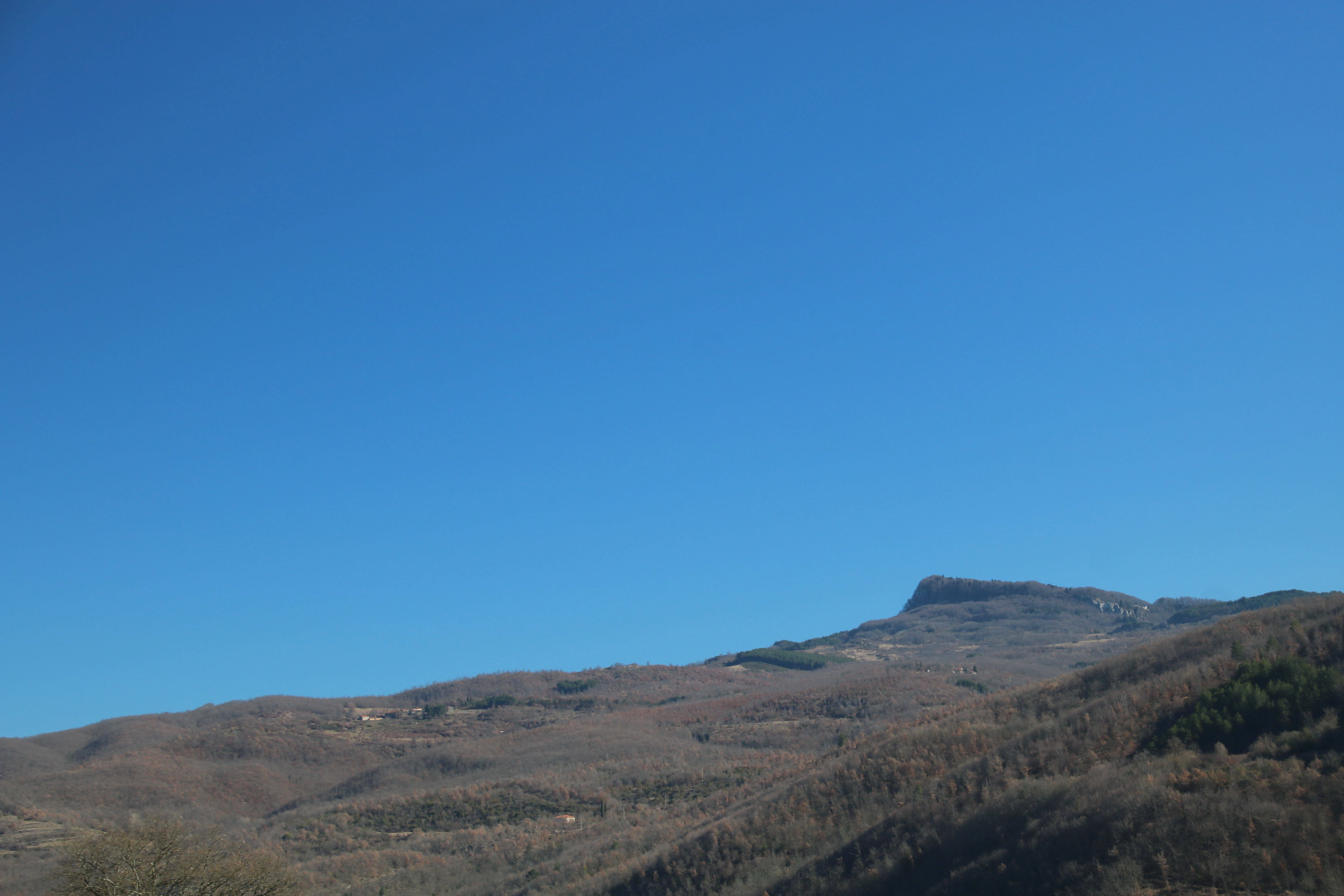 Clear blue sky above rolling hills and a distant mountain peak in a mountainous landscape