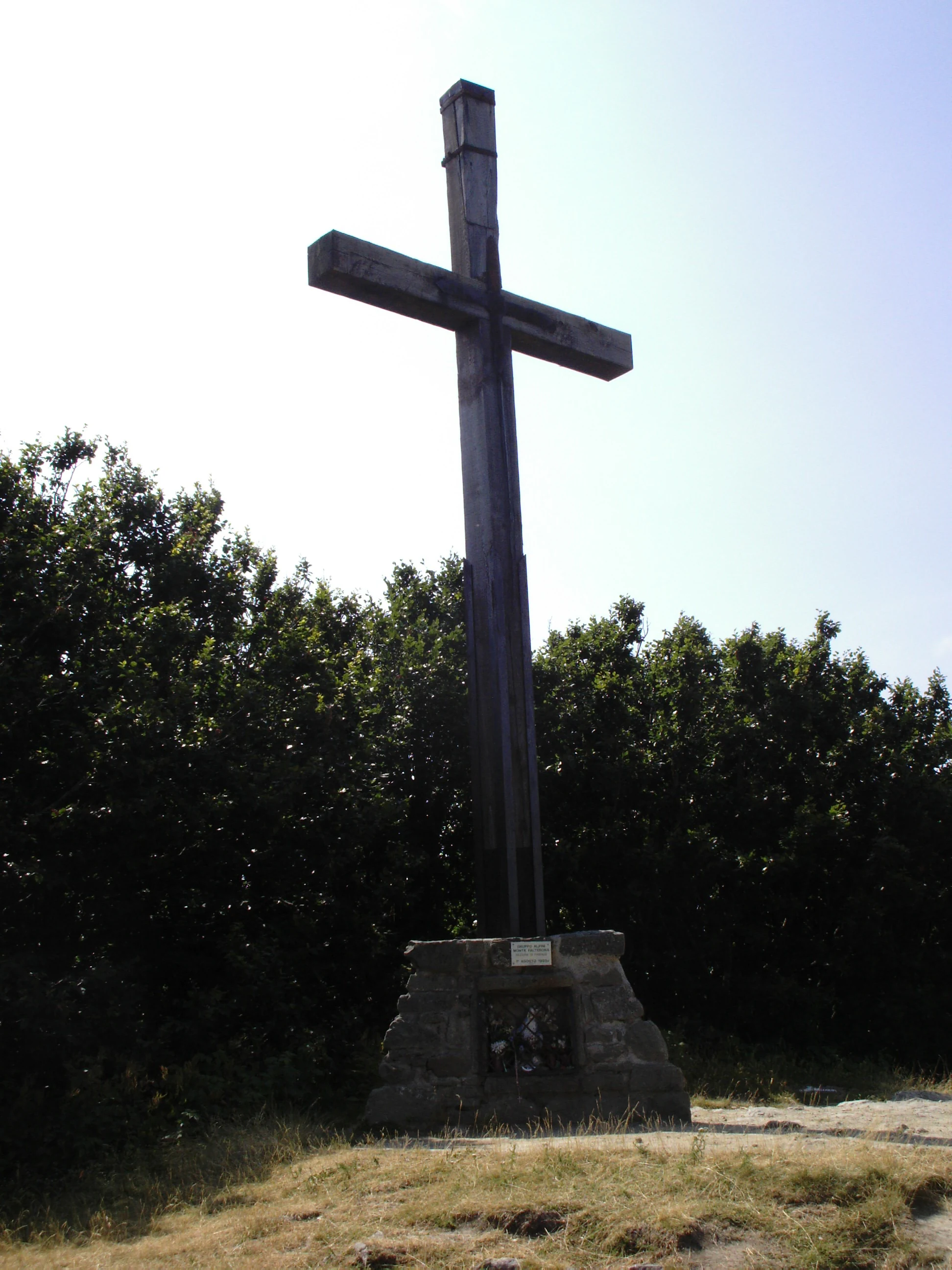 Tall wooden cross on a stone base with trees and clear sky in the background