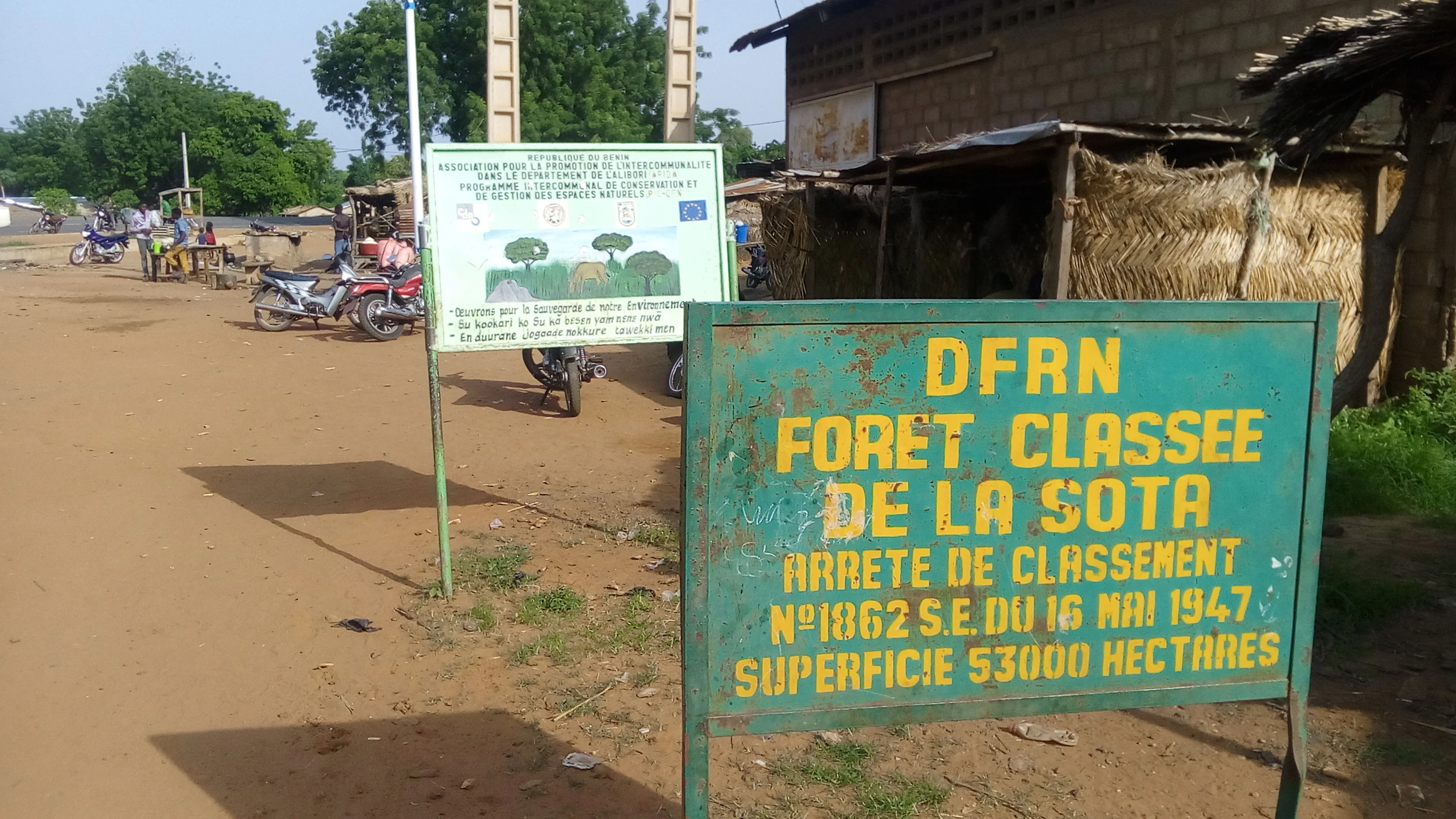 A green metal sign with yellow text reading DFRN FORET CLASSEE DE LA SOTA, along with information about its 1947 legal classification and 53,000 hectare surface area, set in an outdoor dirt area near another informational board.