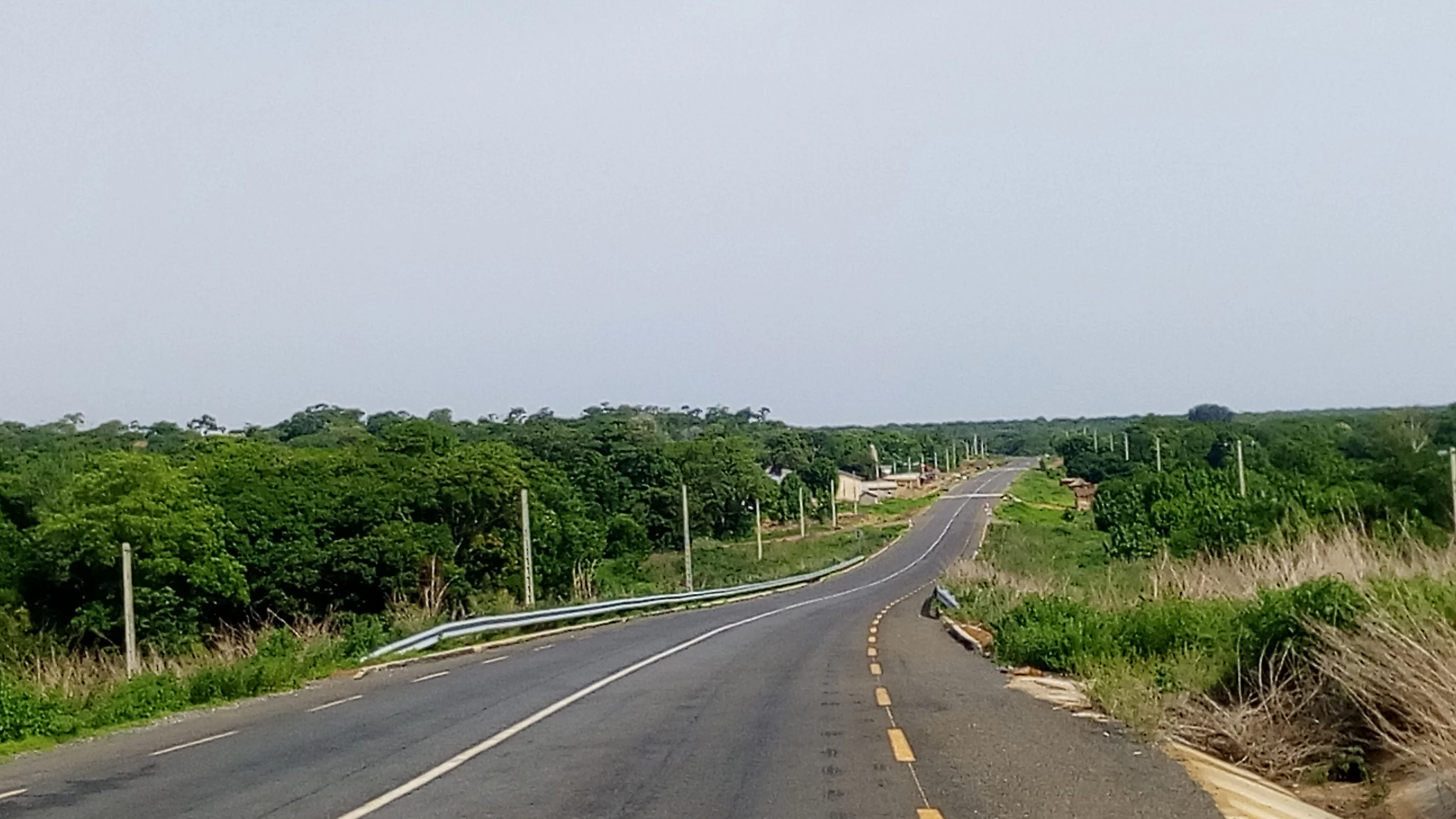 A view from a vehicle driving on a paved highway that cuts through a dense green forest and savanna landscape in Benin.