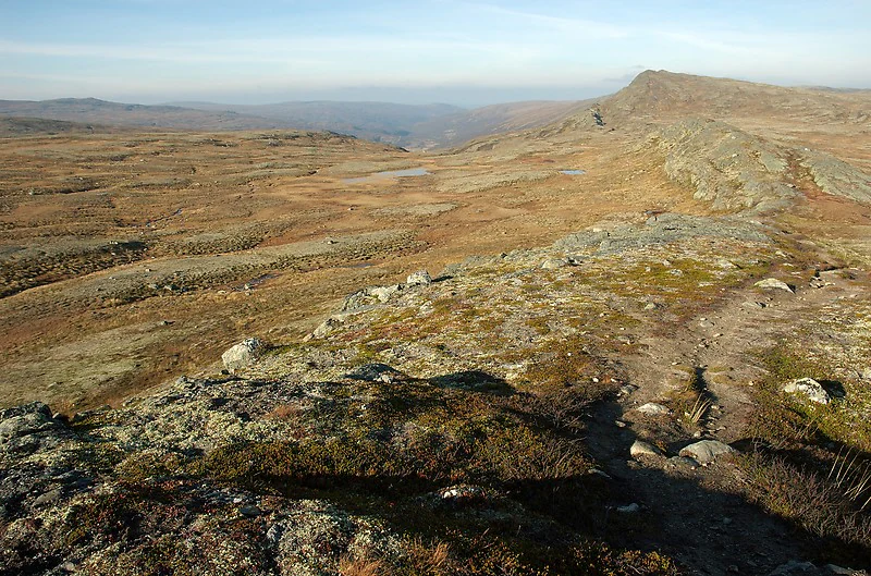 Panoramic alpine landscape with rocky terrain and trail leading to distant mountains under clear sky