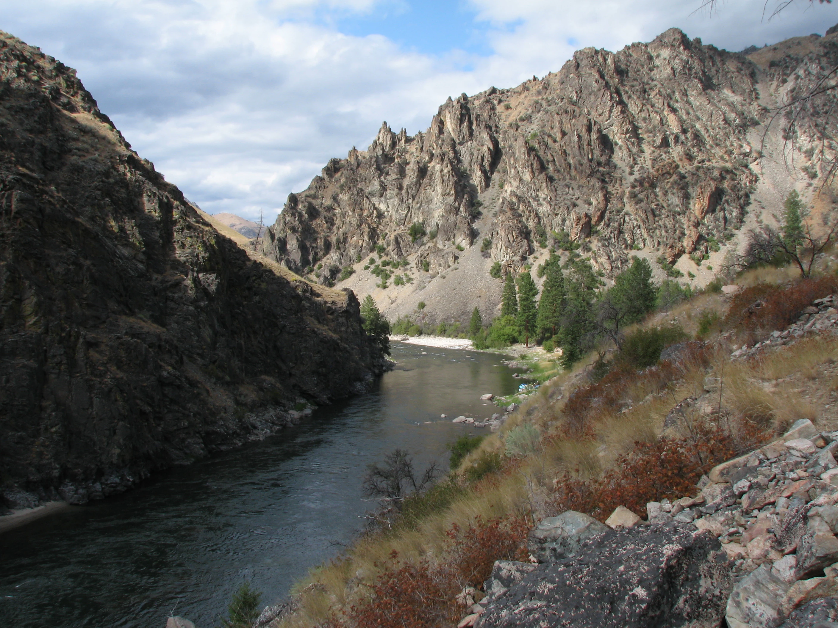 A wide shot looking down a river canyon with steep, rocky cliffs on both sides and a flowing river in the center.