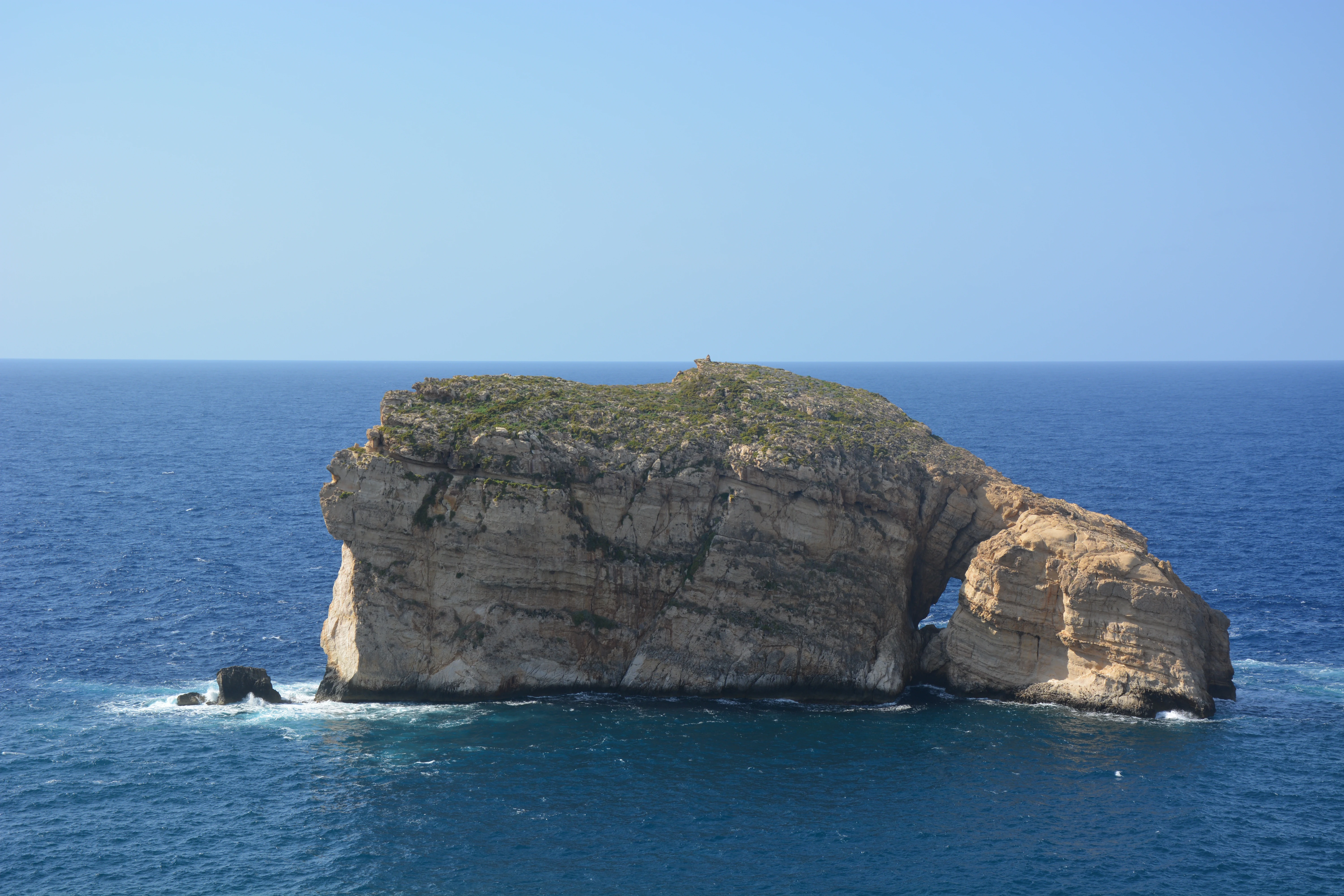 A limestone islet rising from deep blue Mediterranean waters under a clear sky.
