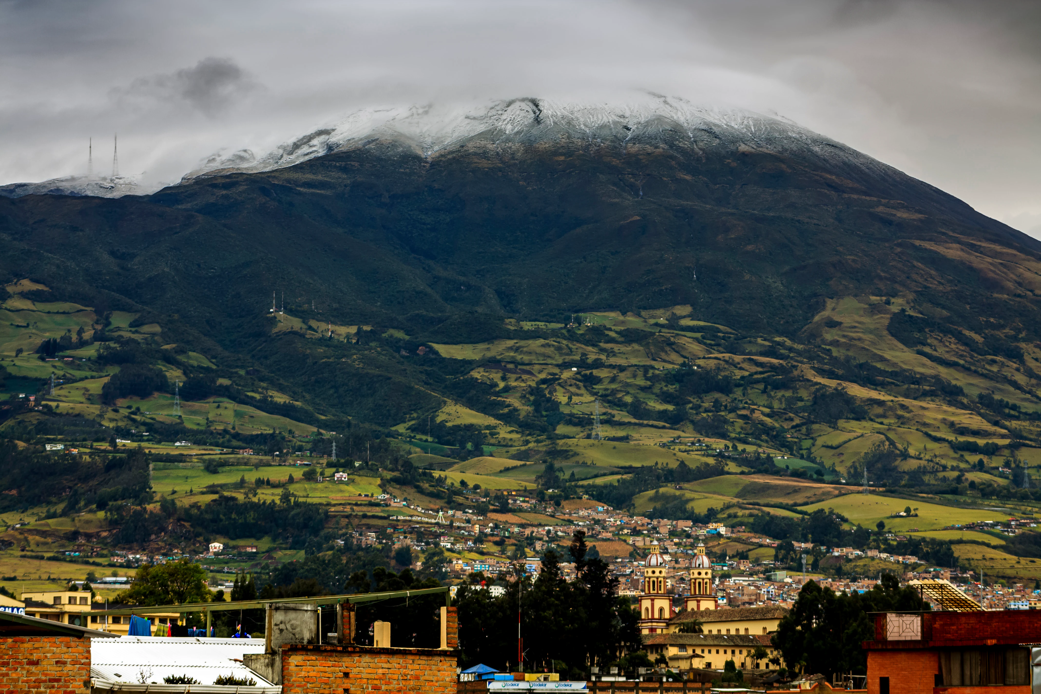 Snow-capped Galeras Volcano with green hills and city of Pasto in foreground under cloudy sky